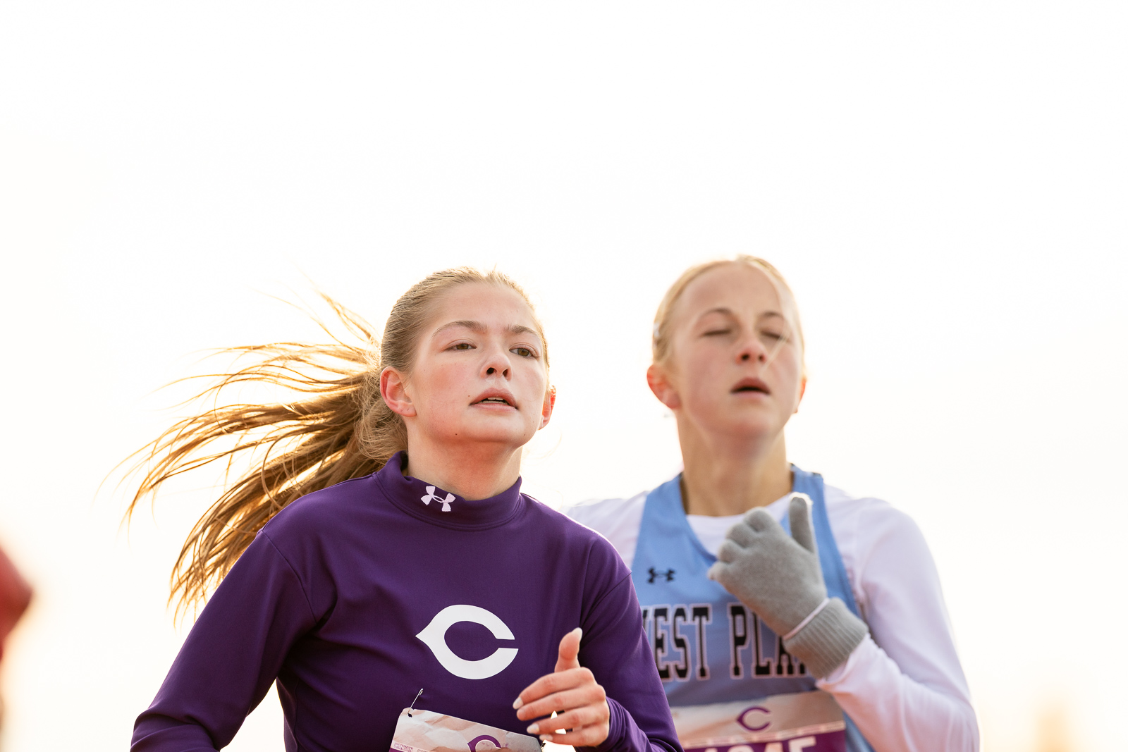 canyon-eagles-district-xc-jpegJoe-pps-10 | Press Pass Sports Two young female runners race side by side outdoors, wearing numbered bibs and athletic jerseys.