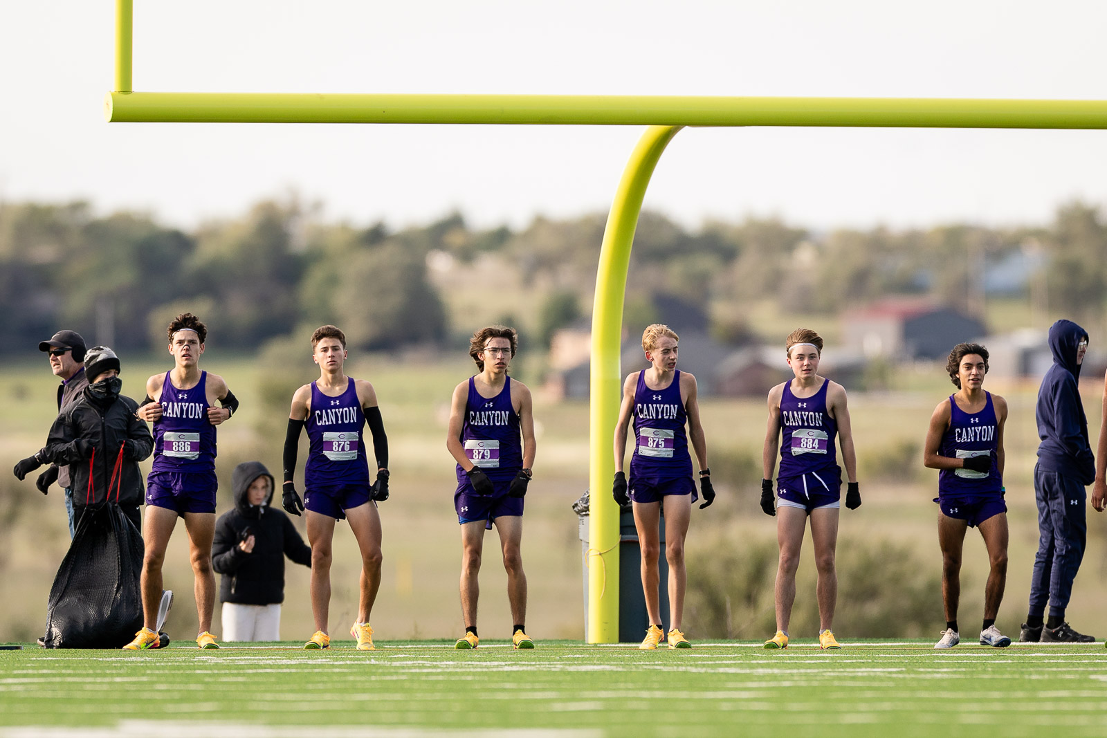 canyon-eagles-district-xc-jpegJoe-pps-12 | Press Pass Sports Seven runners in purple Canyon uniforms line up at the track start beneath a bright yellow goalpost, ready to race.