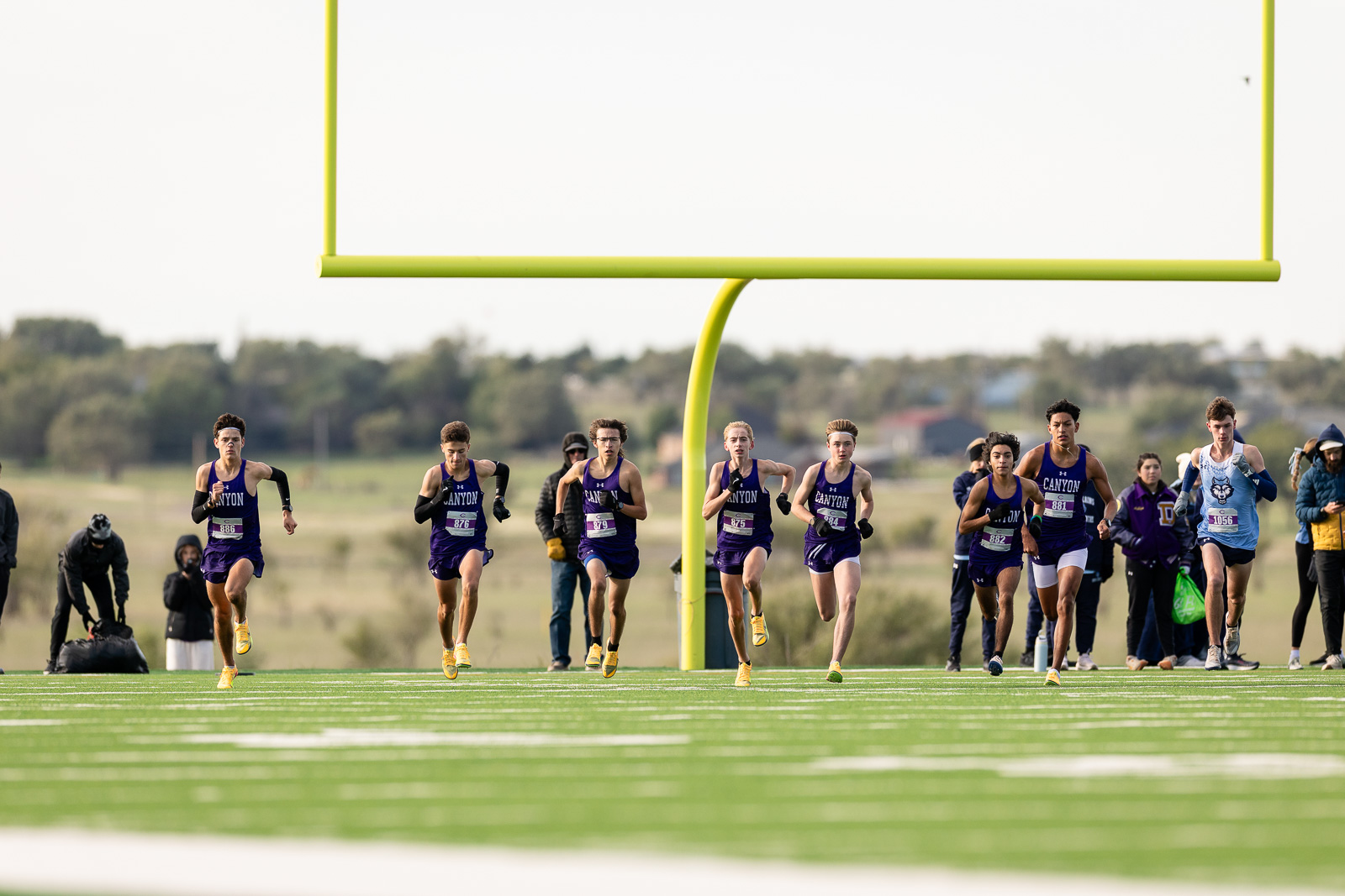 canyon-eagles-district-xc-jpegJoe-pps-13 | Press Pass Sports Runners sprint toward the finish line on a football field, framed by a large yellow goalpost in the background.