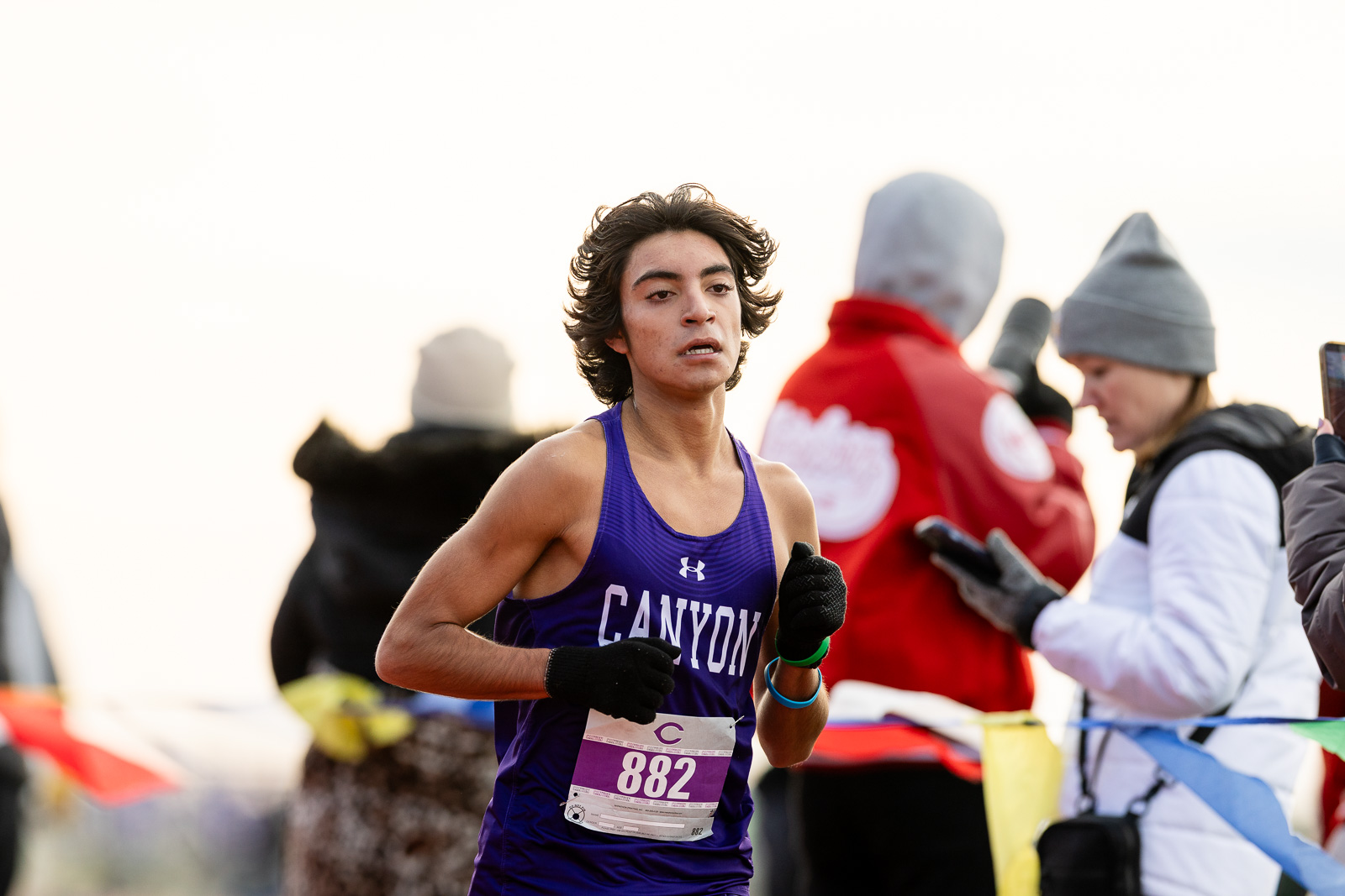 canyon-eagles-district-xc-jpegJoe-pps-15 | Press Pass Sports Female runner in a purple Canyon singlet with bib 882, mid-race, with spectators and volunteers in the background.