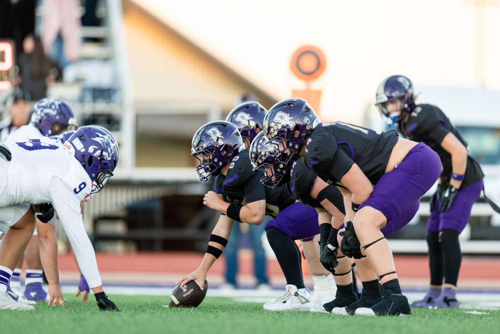 spearman-vs-panhandle-football-jpegJoe-pps-1 | Press Pass Sports Football players in black and purple prepare at the line of scrimmage as the center snaps the ball down the line of scrimmage in a game setting
