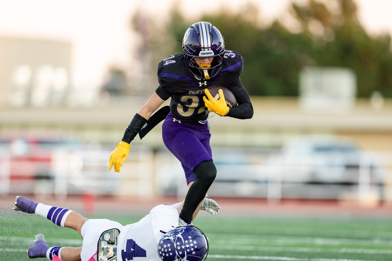 spearman-vs-panhandle-football-jpegJoe-pps-3 | Press Pass Sports Football player in purple and black with yellow gloves carries the ball, leaping over a defender on a green field show action.