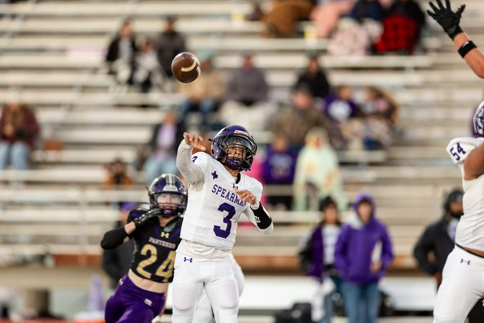 spearman-vs-panhandle-football-jpegJoe-pps-9 | Press Pass Sports Quarterback in white number 3 throws a pass as a defender closes in during a football game, with bleachers in the background.