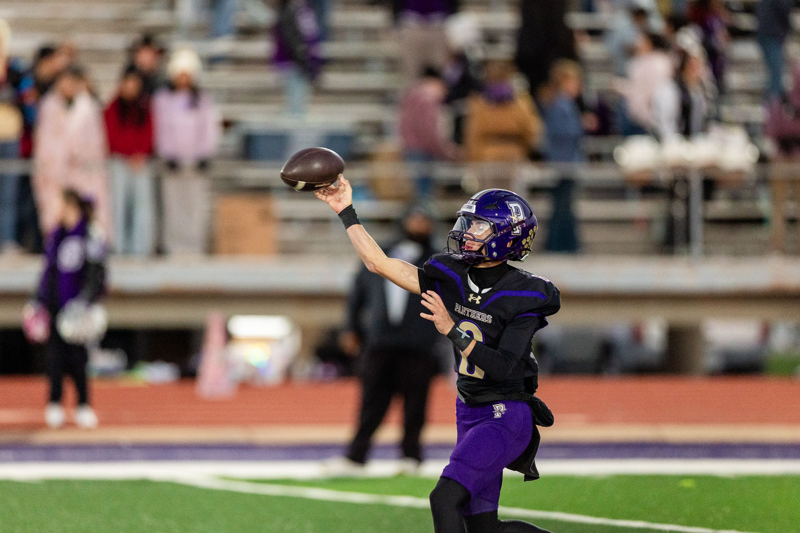 spearman-vs-panhandle-football-jpegJoe-pps-12 | Press Pass Sports Football quarterback in purple and black uniform throwing a pass on a turf field with stands and spectators in the background.