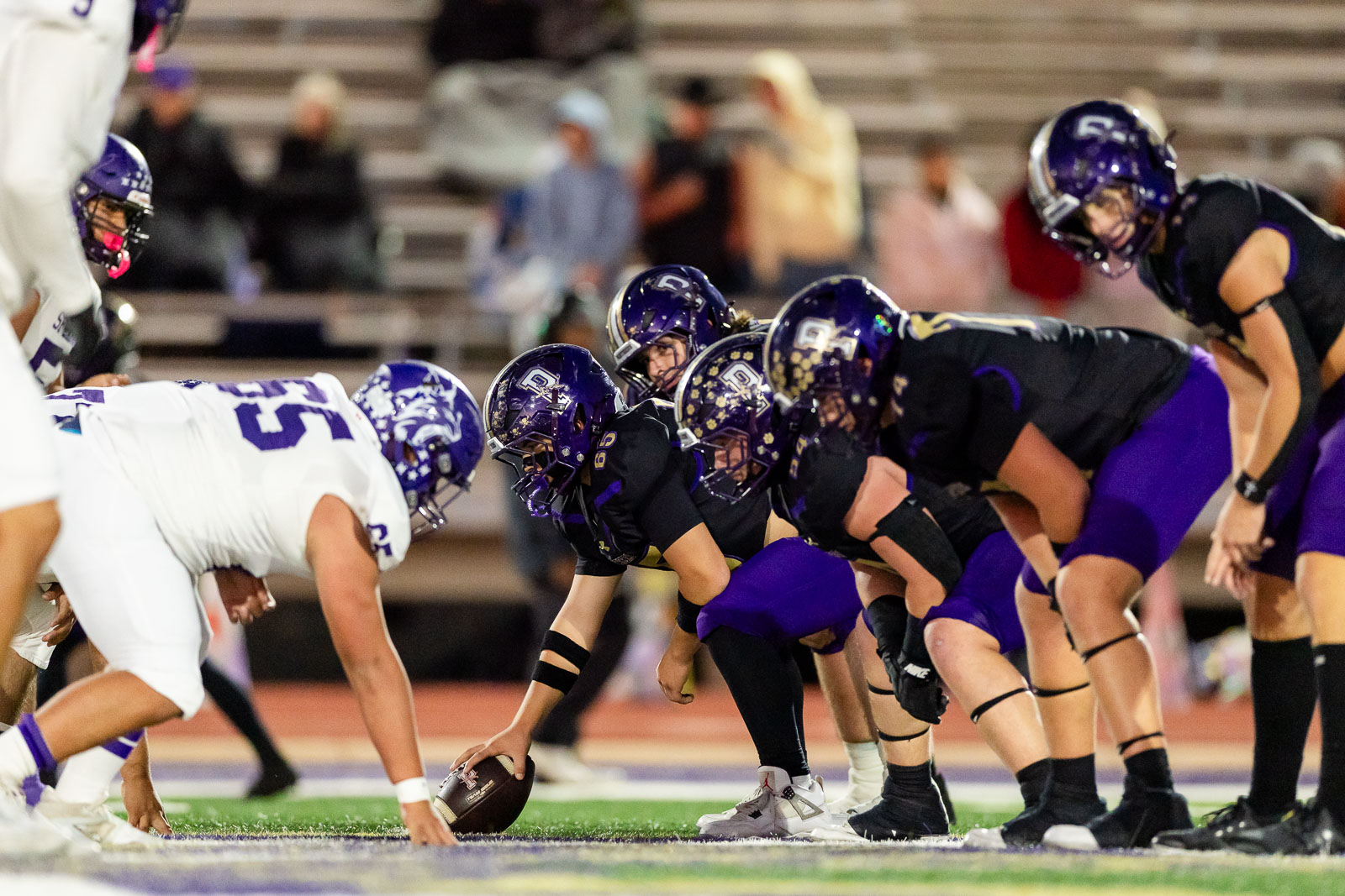 spearman-vs-panhandle-football-jpegJoe-pps-13 | Press Pass Sports Football players line up at the line of scrimmage during a play, centers ready to snap the ball between white and purple uniforms
