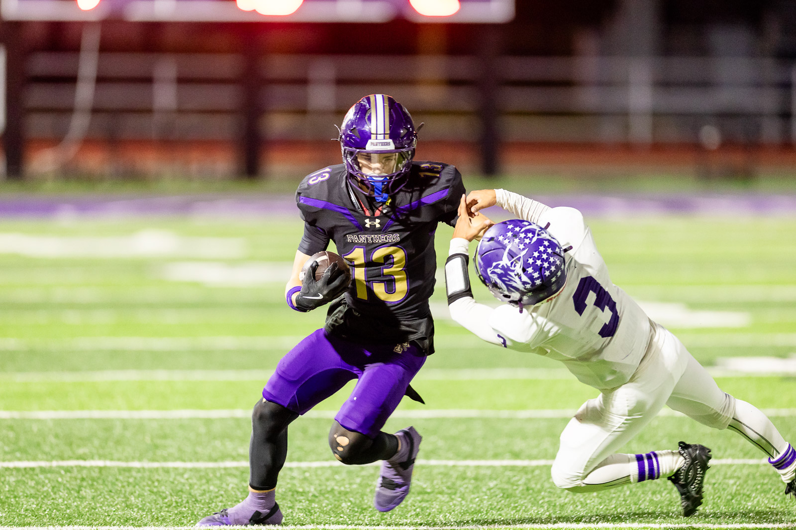 spearman-vs-panhandle-football-jpegJoe-pps-16 | Press Pass Sports American football player in black-purple Panthers uniform (number 13) runs with ball while a white-uniform defender dives to tackle him on a green field.