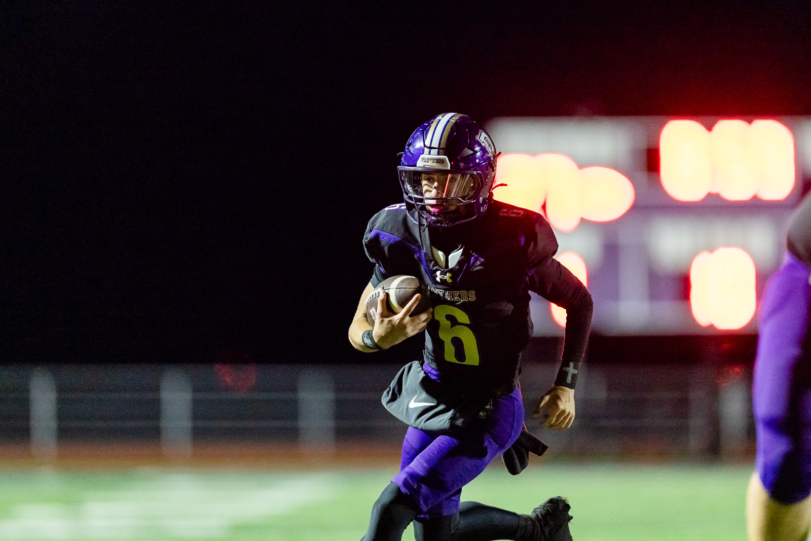 spearman-vs-panhandle-football-jpegJoe-pps-27 | Press Pass Sports Football player in a black and purple uniform running with the ball at night, wearing number 6 and a purple helmet.