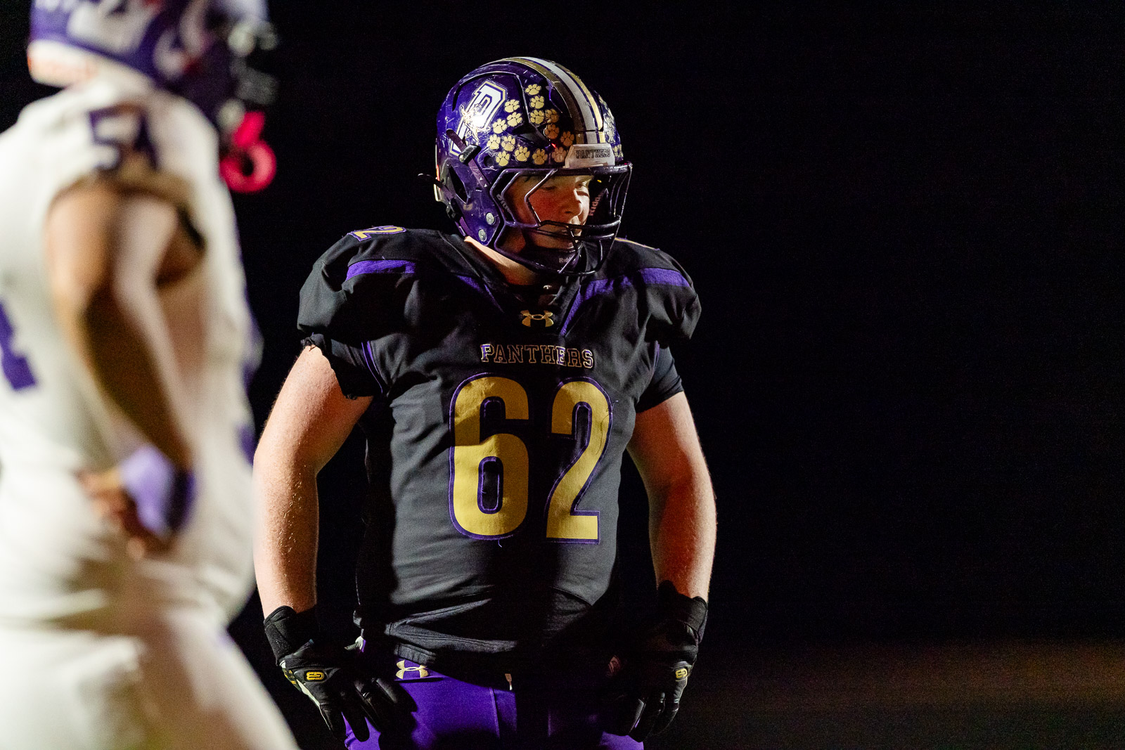 spearman-vs-panhandle-football-jpegJoe-pps-28 | Press Pass Sports Football player in black and purple Panthers uniform with number 62 stands on a night field, hands on hips, helmet on.