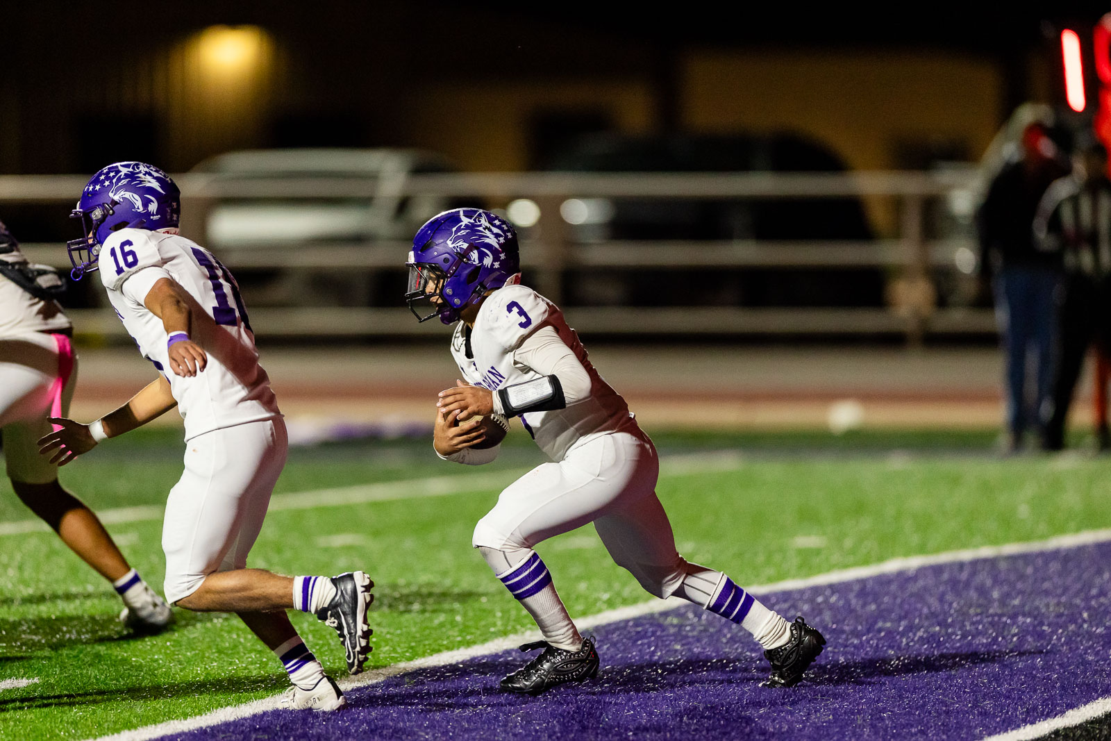 spearman-vs-panhandle-football-jpegJoe-pps-29 | Press Pass Sports Football player wearing white and purple, number 3, runs with the ball on a night game on a purple and green turf field.