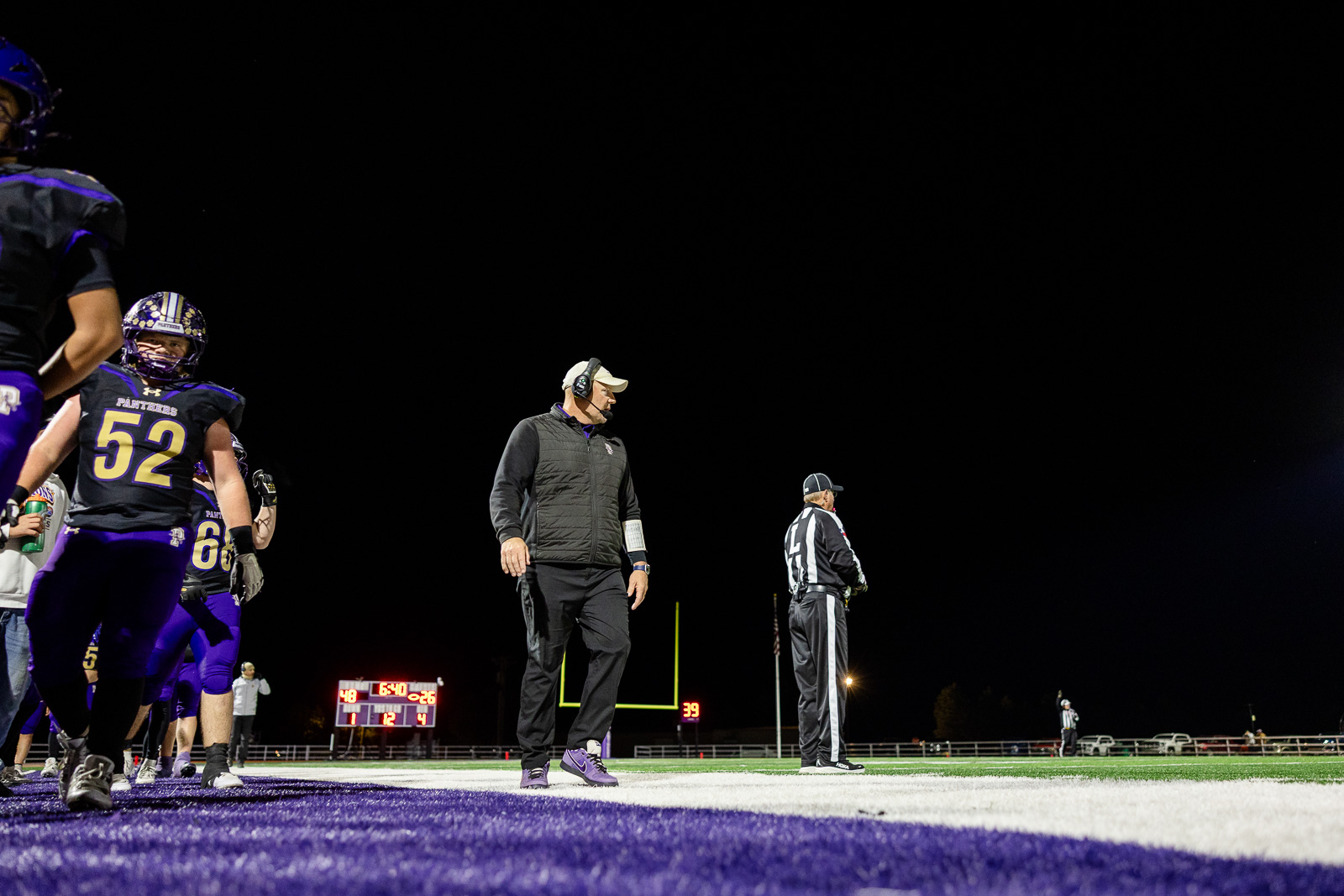 spearman-vs-panhandle-football-jpegJoe-pps-36 | Press Pass Sports Nighttime football sidelines with players in purple uniforms and a coach wearing a headset on the field edges.