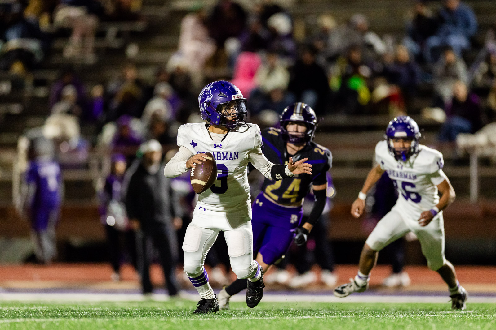 spearman-vs-panhandle-football-jpegJoe-pps-37 | Press Pass Sports Football player in white uniform (number 3) runs with the ball while being chased by purple-clad defenders on a night game field.