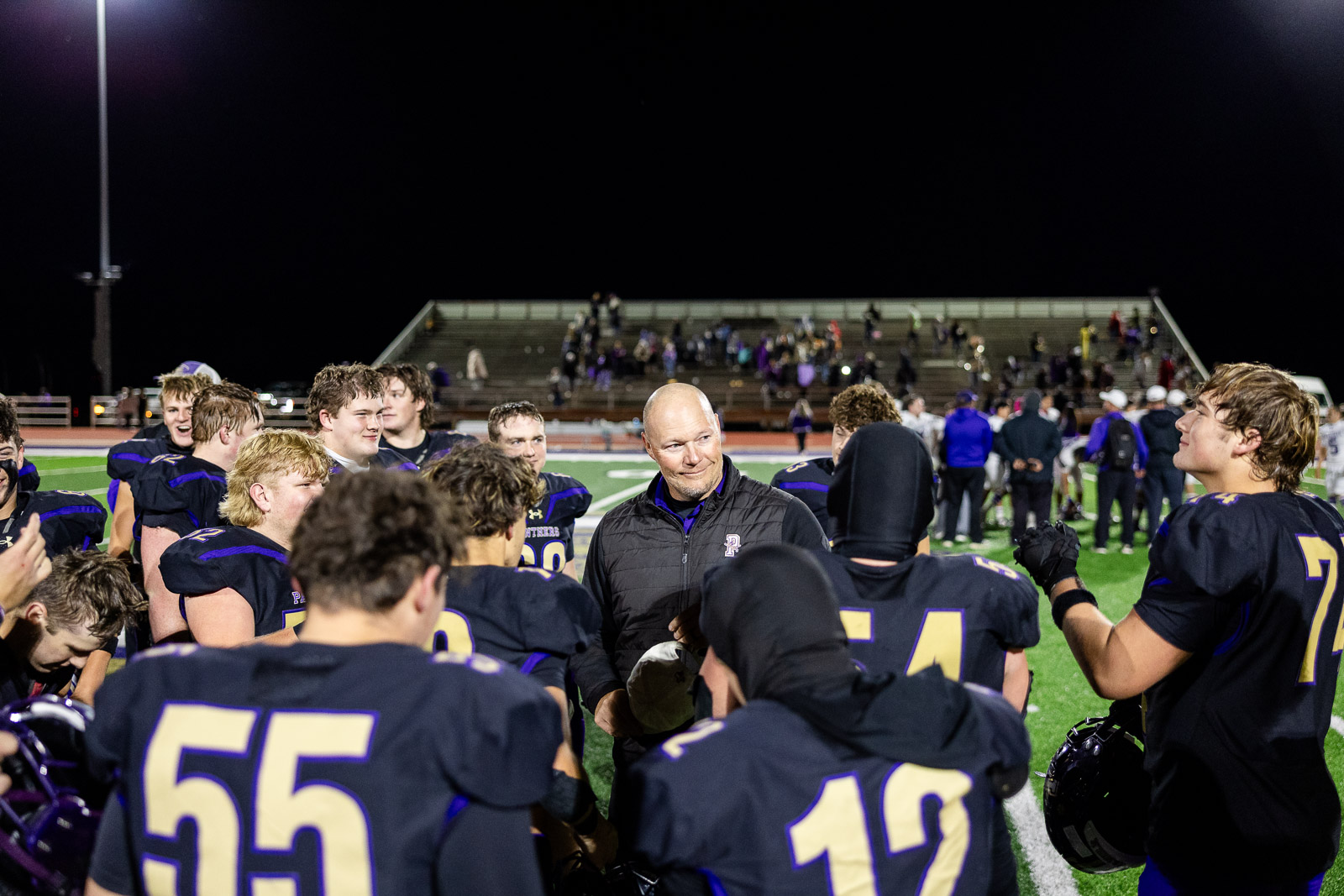 spearman-vs-panhandle-football-jpegJoe-pps-43 | Press Pass Sports Football coach speaks to his players in a huddle on the night football field under stadium lights.