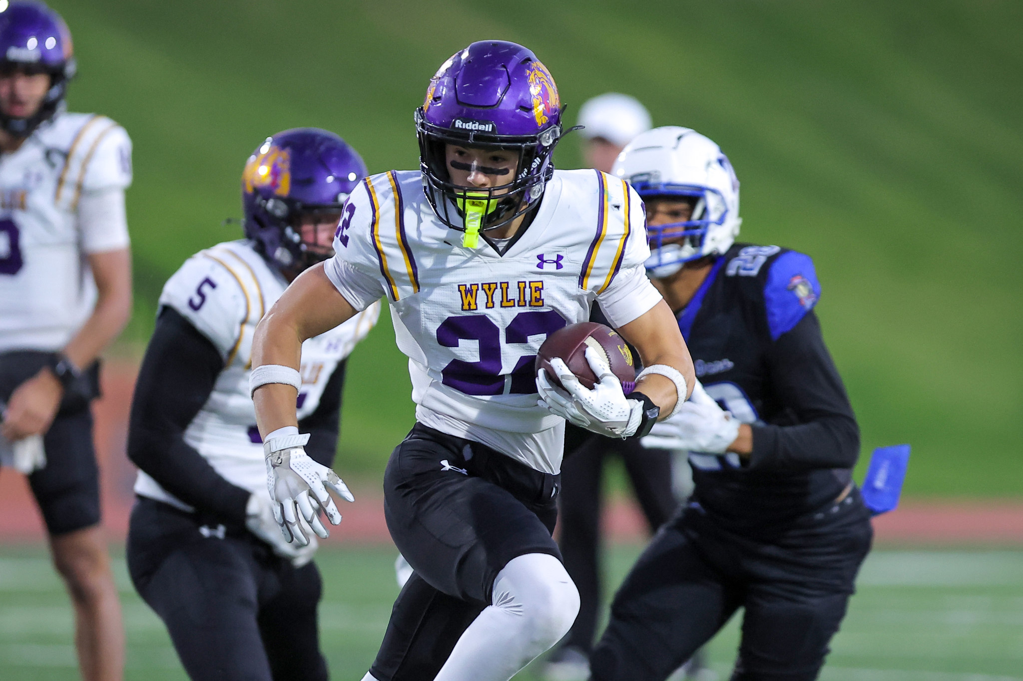 Player in white and purple football jersey numbered 31 runs with ball during a game; defenders in background on a green field.