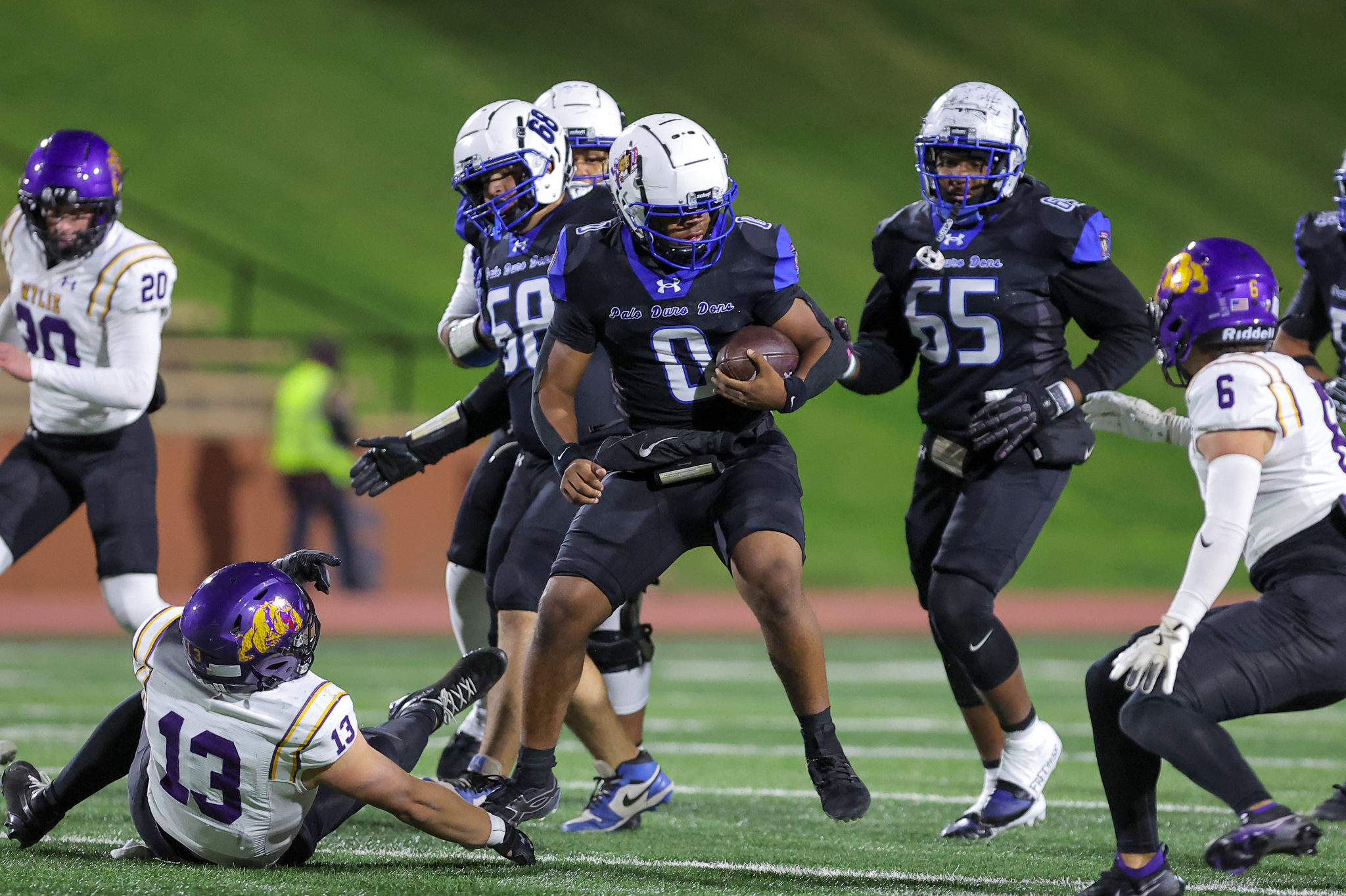 Mid-action football game: a ball-carrier in black dodges tackles while teammates close in around him.