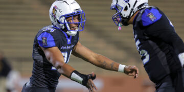 Two football players in blue and black uniforms collide mid‑play on the field.