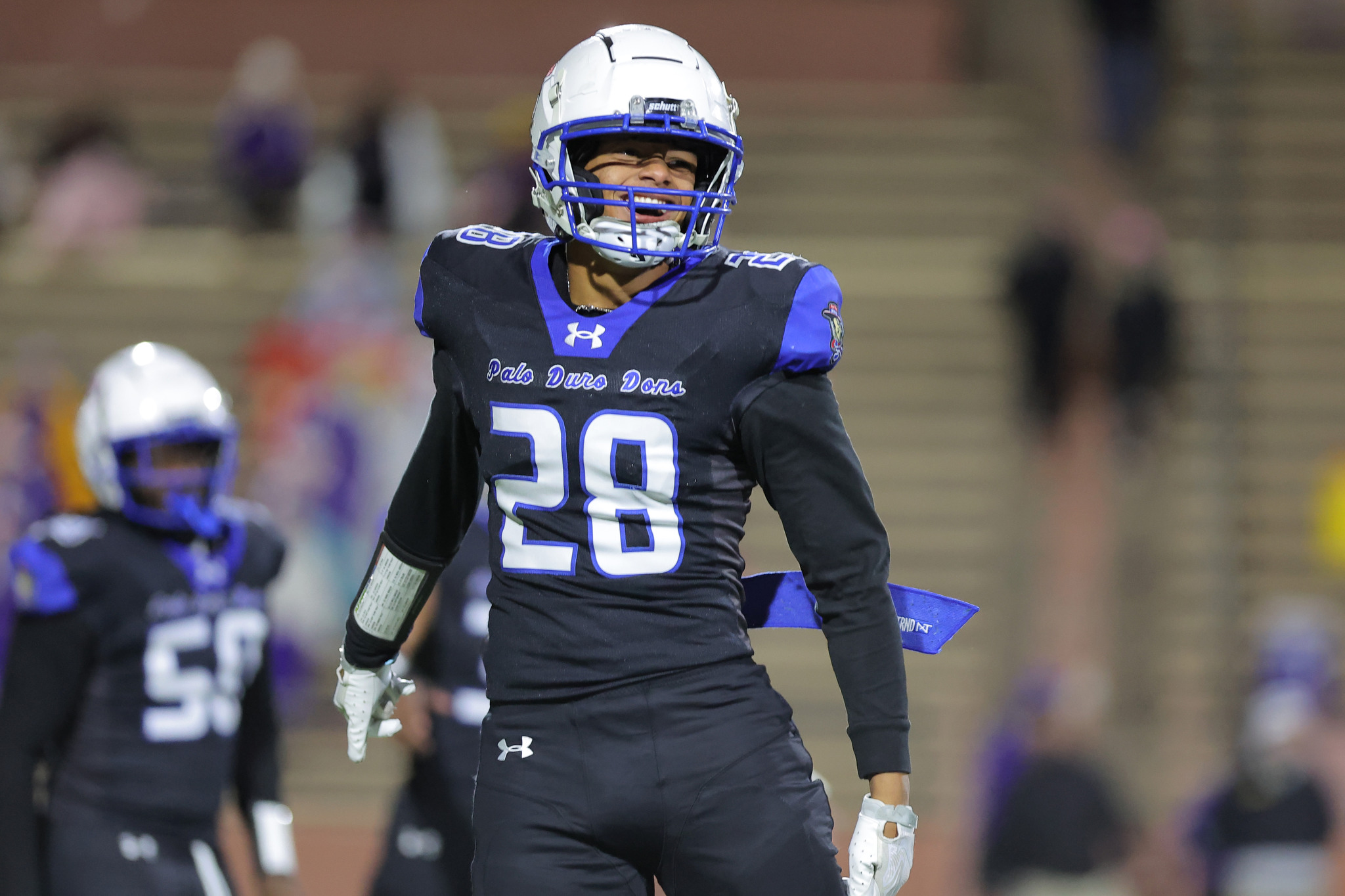 Football player in a black and blue uniform wearing a white helmet with blue face mask, number 28, on a football field.