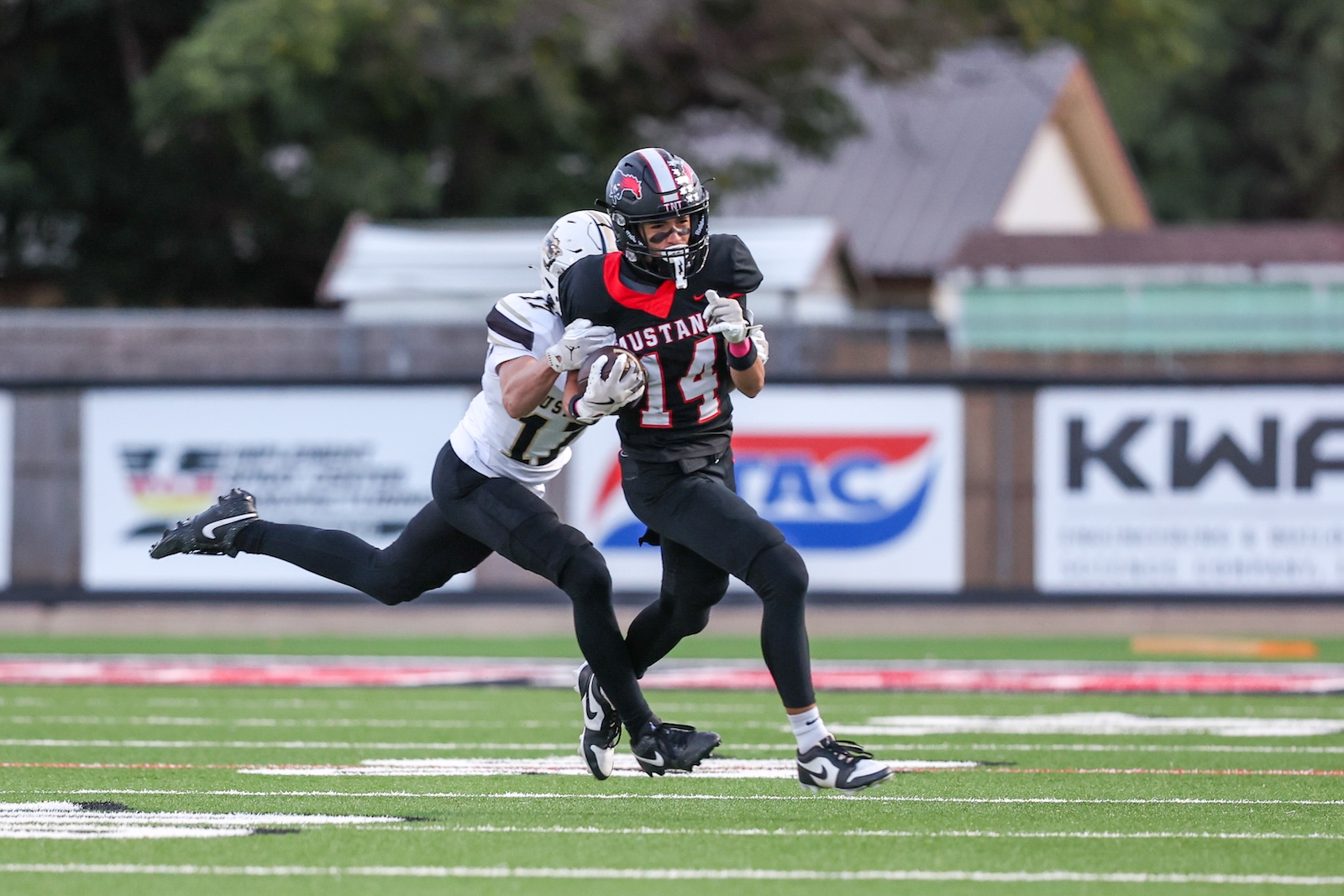 Seabolt Chase-16065 | Press Pass Sports Football player wearing black Mustang jersey with ball, sprinting down the field pursued by a defender in white jersey