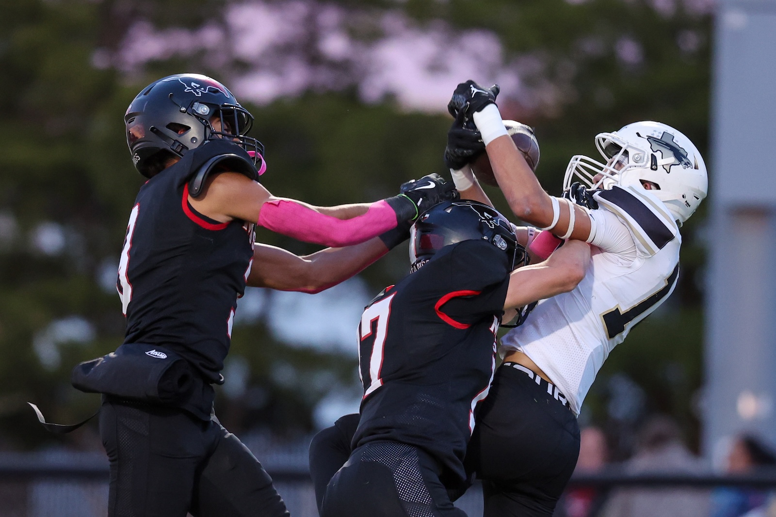 Seabolt Chase-16474 | Press Pass Sports Football players collide as two black-jersey players tackle a white-jersey opponent mid-air on the field during a game.