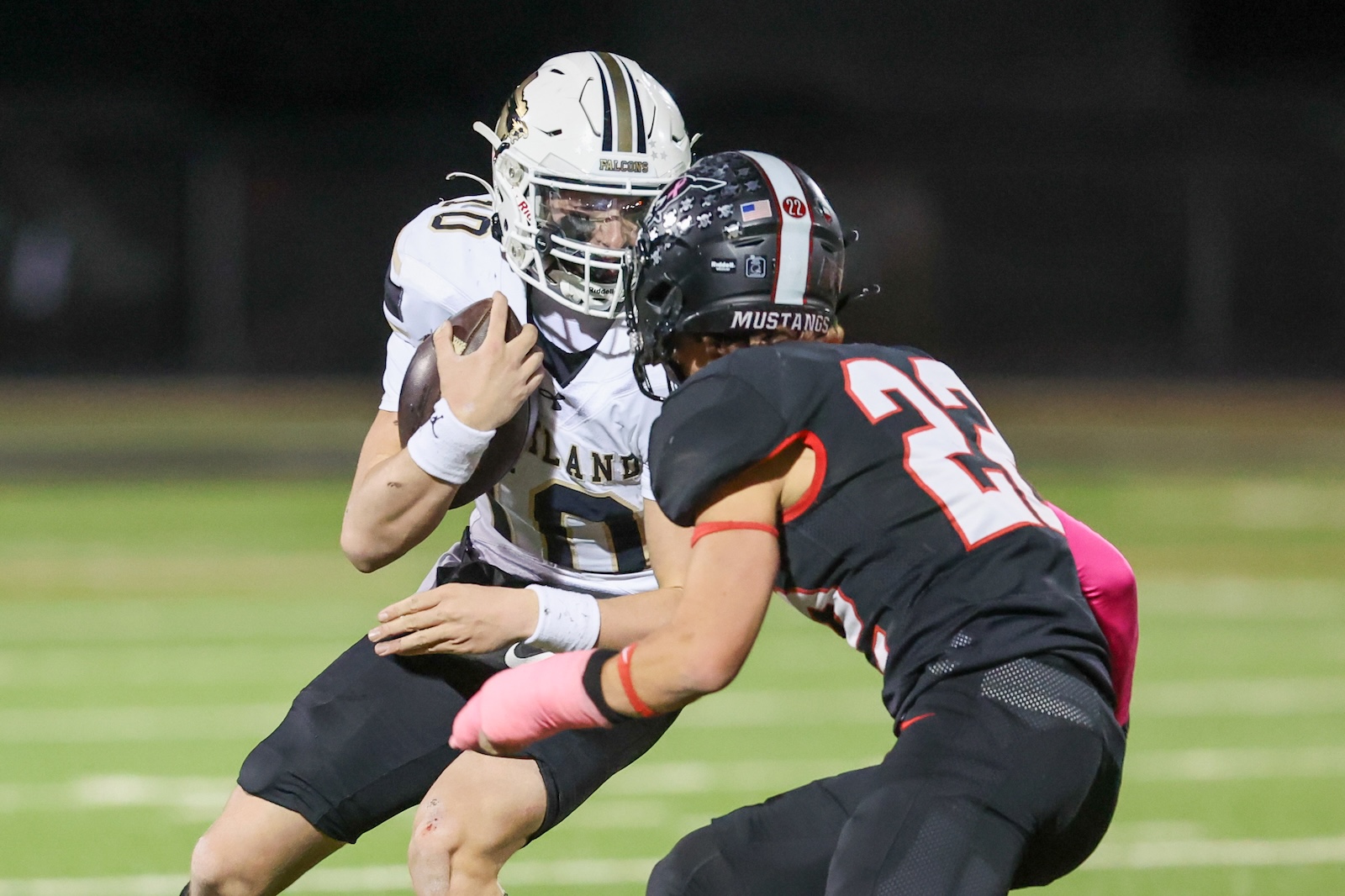 Seabolt Chase-16908 | Press Pass Sports A football player in a white uniform holding the ball is tackled by a defender in a black uniform with the word Mustangs on the helmet.