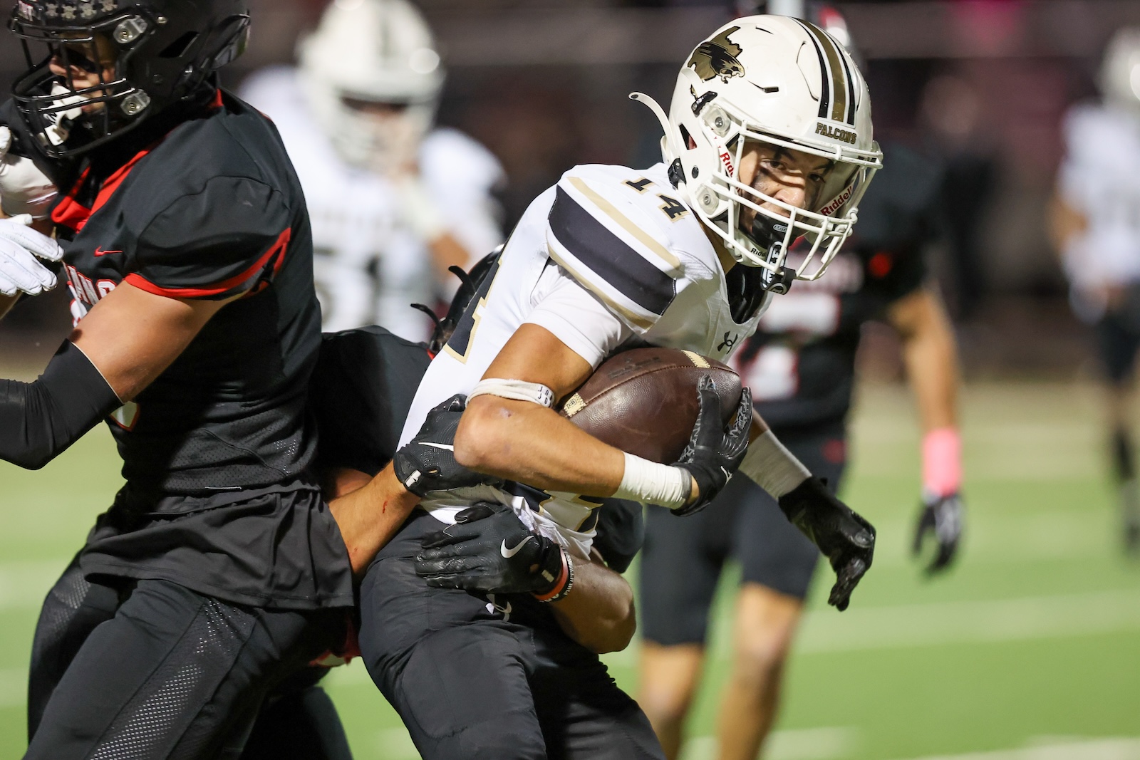 Seabolt Chase-16959 | Press Pass Sports Football player in a white Falcons jersey clutches the ball while a defender in black tackles him on the field at night game.