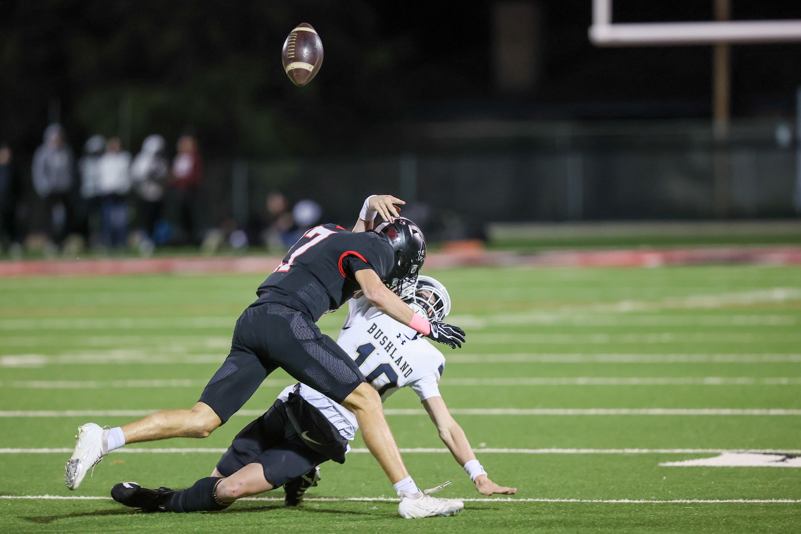 Seabolt Chase-17161 | Press Pass Sports Two football players clash on a bright field as a ball sails overhead during a night game.