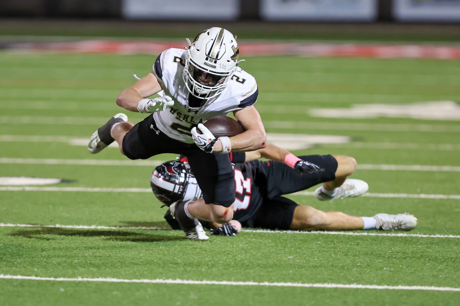 Seabolt Chase-17184 | Press Pass Sports Football player in white jersey carrying the ball dives forward while a defender in black falls behind on a green turf field.