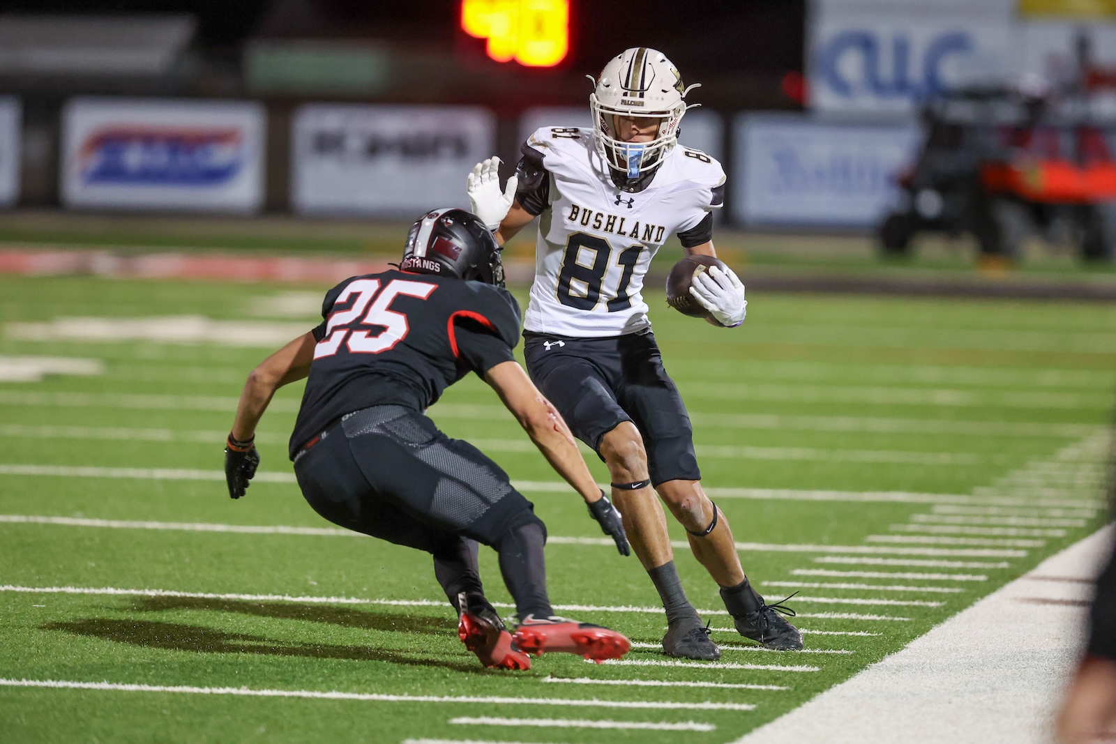 Seabolt Chase-17198 | Press Pass Sports Bushland player in white jersey (81) runs with the football as a defender in black (#25) closes in on the field at night.