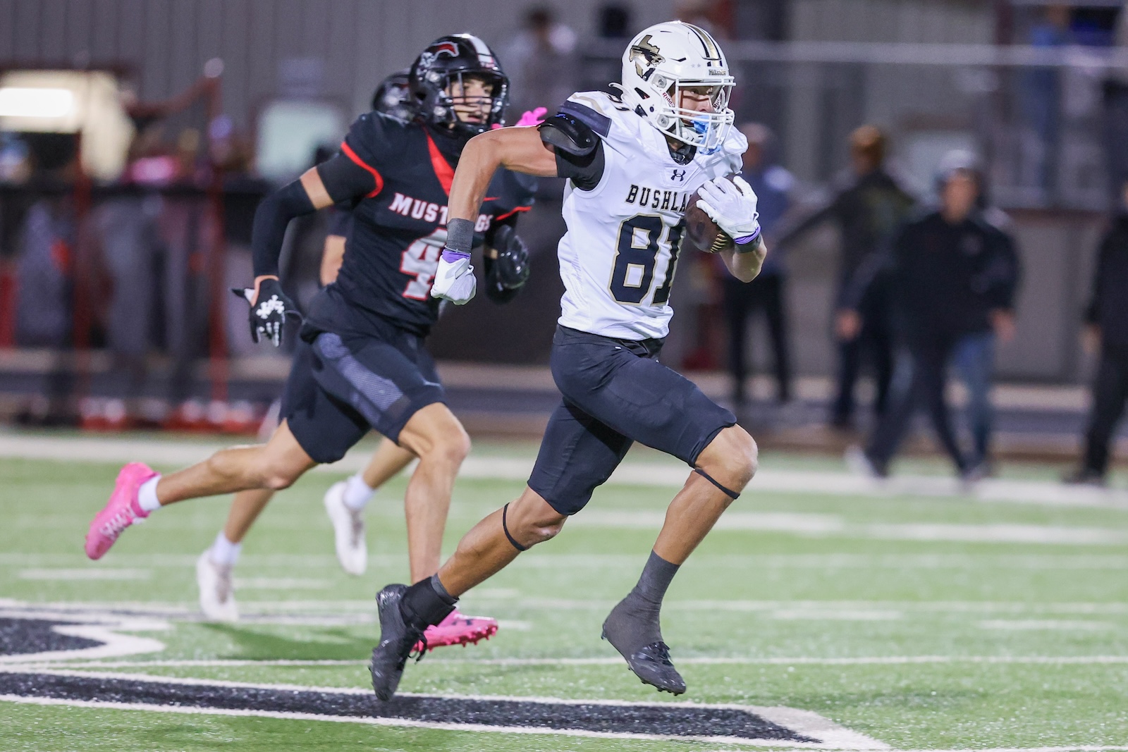 Seabolt Chase-17561 | Press Pass Sports Football player in white jersey (#81) carries the ball and sprints down the field as a defender in black pursues behind him on the turf.