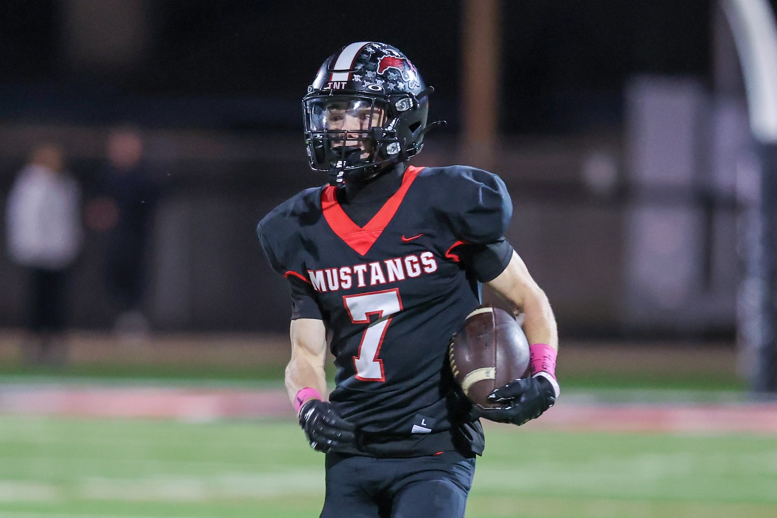 Seabolt Chase-17822 | Press Pass Sports Football player in black 'Mustangs' jersey with number 7, sprinting with the ball at night on a football field.