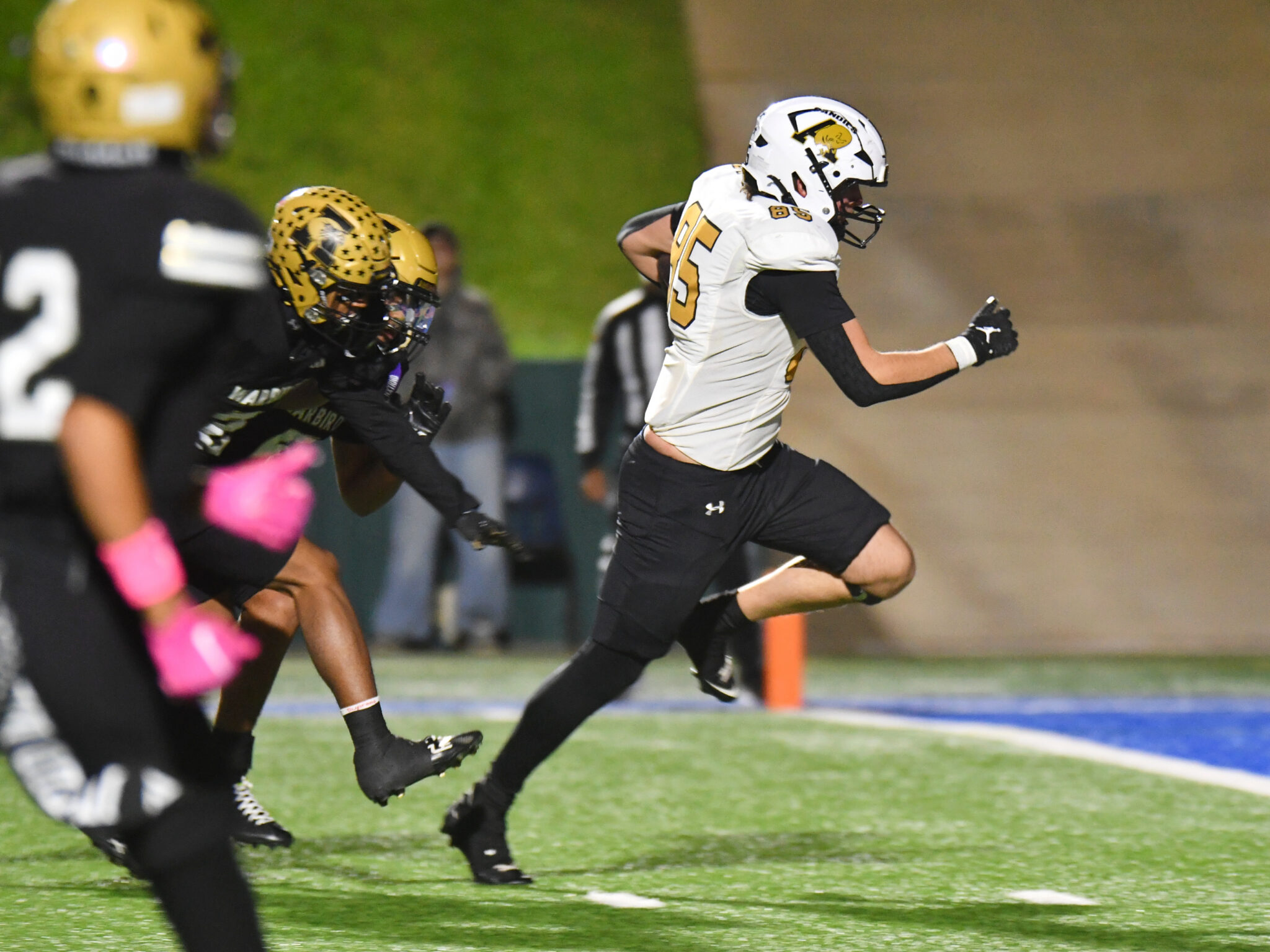 DSC_5375 | Press Pass Sports Football players sprinting on the field during a game, white jersey with number 25 leading the run behind a black-clad opponent in gold helmet