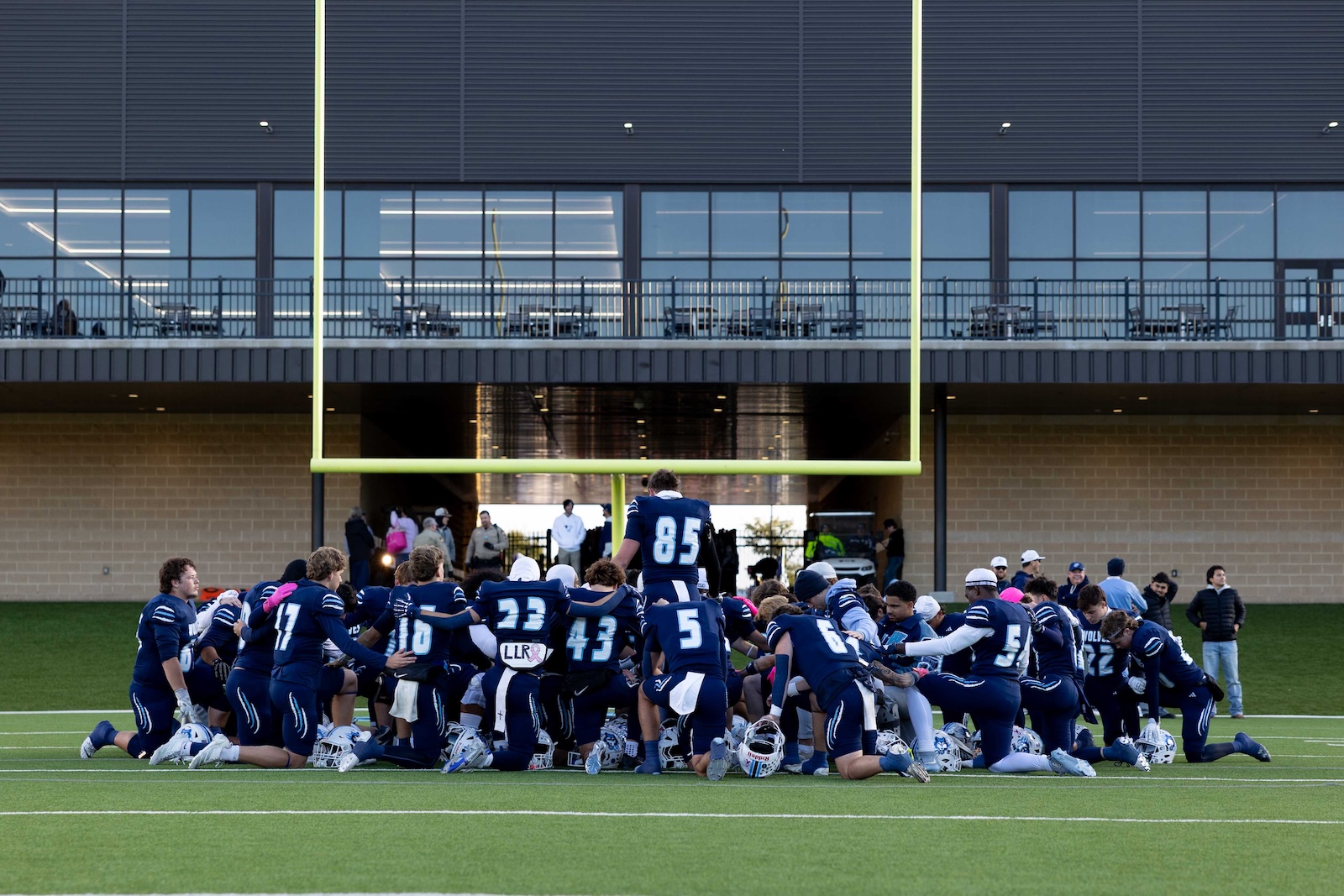 CHS-WPHS-FB-1 | Press Pass Sports Blue-clad football players form a huddle on a green turf field near a bright yellow goalpost.