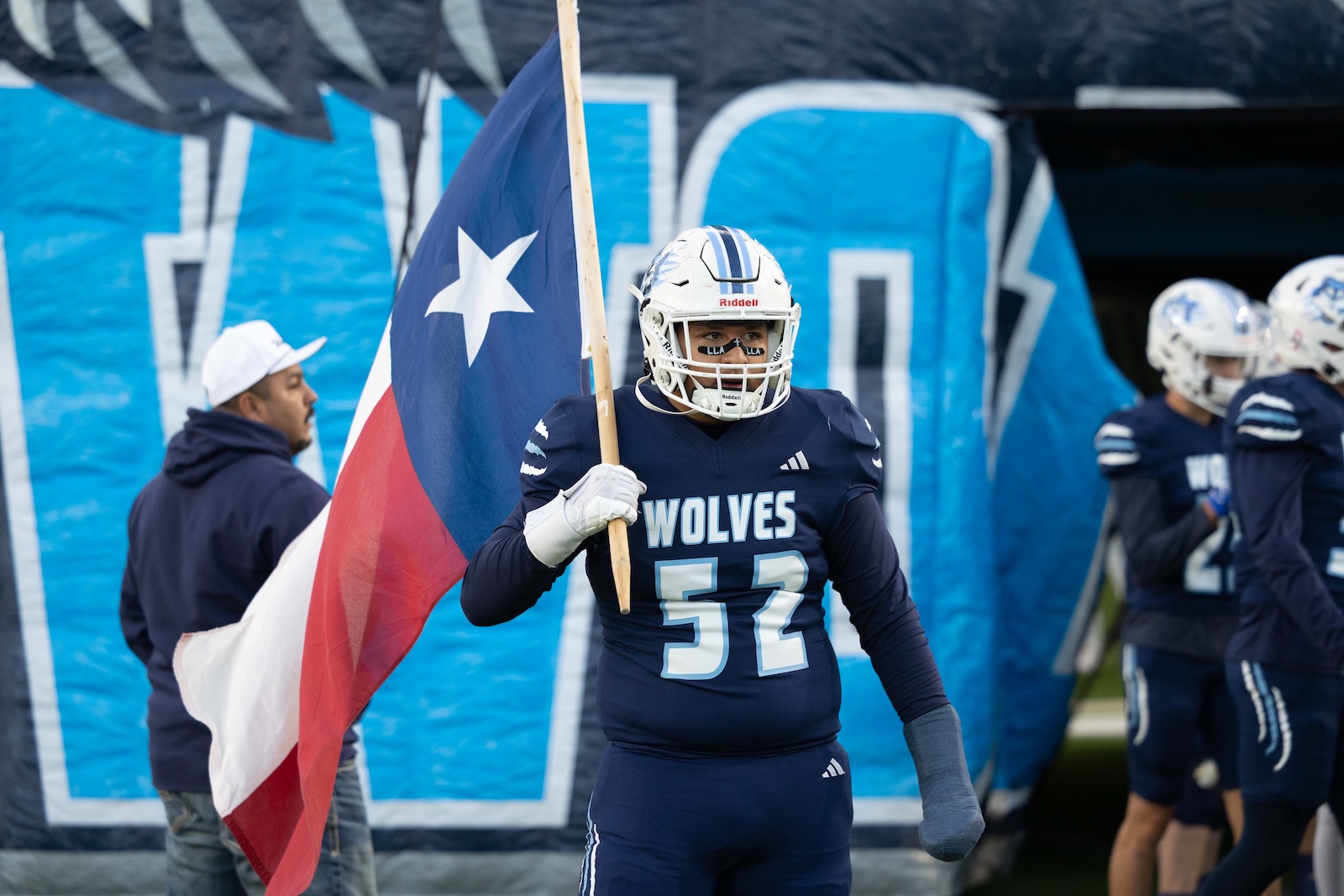 CHS-WPHS-FB-2 | Press Pass Sports American football player in a navy Wolves uniform holding a Texas flag on the field, white helmet with blue stripes and number 52 visible.