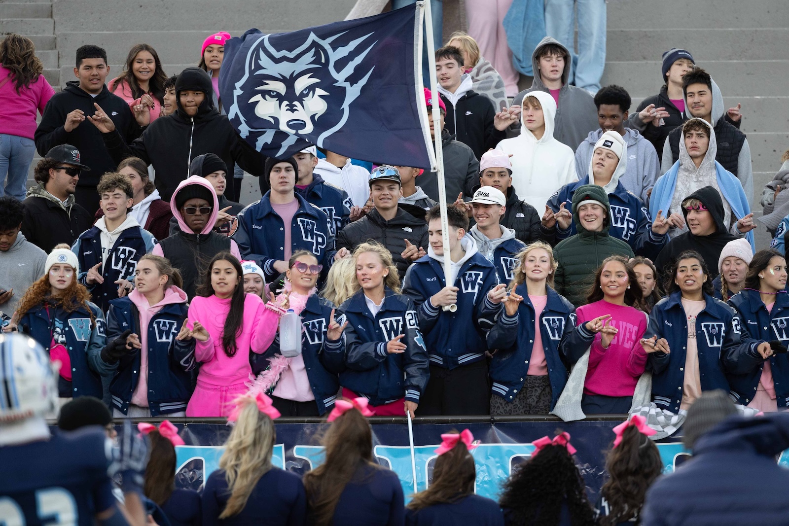 CHS-WPHS-FB-3 | Press Pass Sports Large group of students cheering in bleachers, many wearing blue varsity jackets with a W, and a large wolf flag in the background.