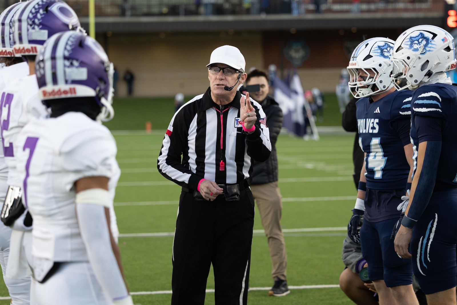CHS-WPHS-FB-7 | Press Pass Sports Football referee in a black-and-white striped uniform with a headset and white cap speaks to players on the field between two teams.