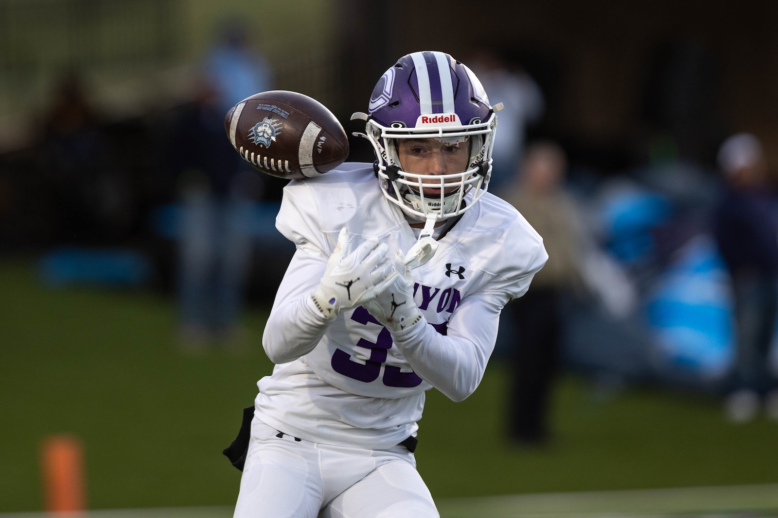 CHS-WPHS-FB-9 | Press Pass Sports Football player in a white uniform reaches to catch a pass, wearing a purple helmet and gloves on a grassy field.
