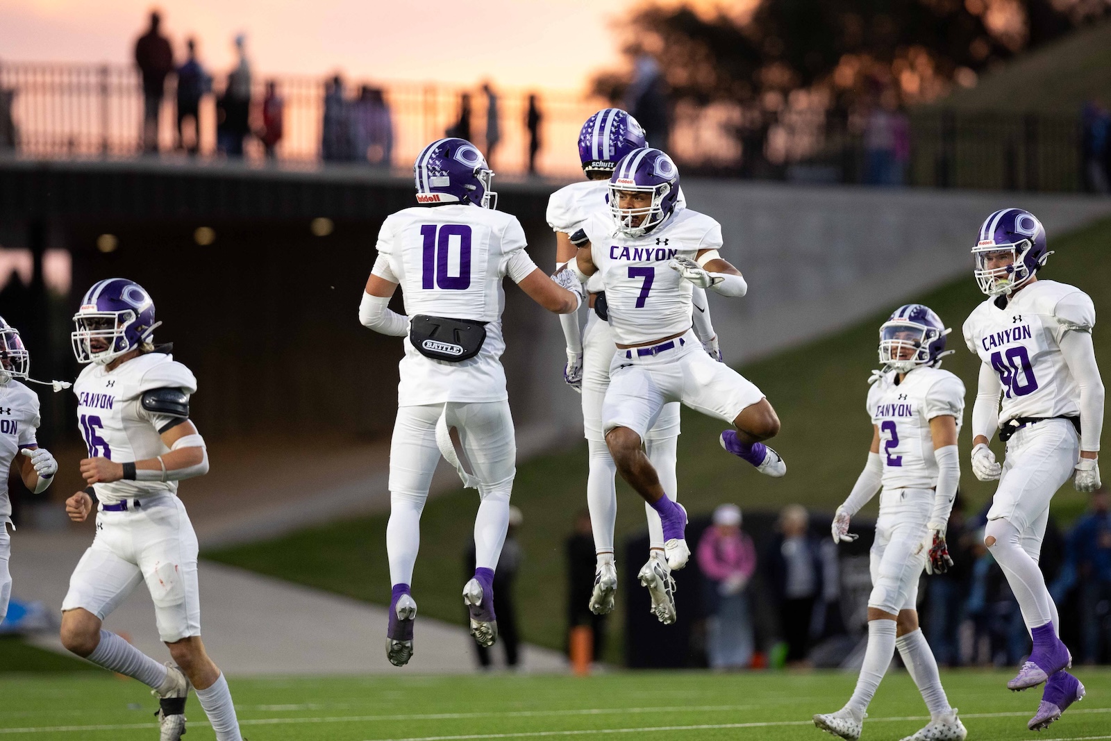 CHS-WPHS-FB-16 | Press Pass Sports Canyon football players in white and purple celebrate by leaping in the end zone as teammates run toward them.