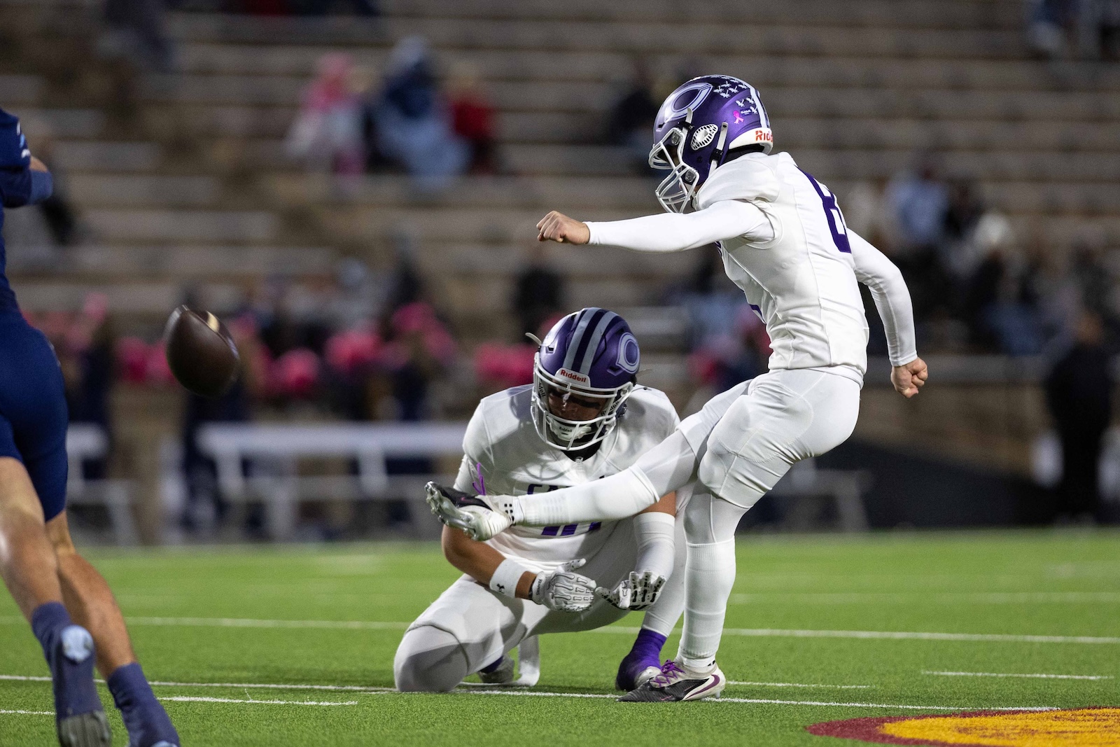 CHS-WPHS-FB-18 | Press Pass Sports Two football players in white uniforms collide on a green field as one jumps near the ball midair while a teammate on the ground reaches forward for the ball nearby.