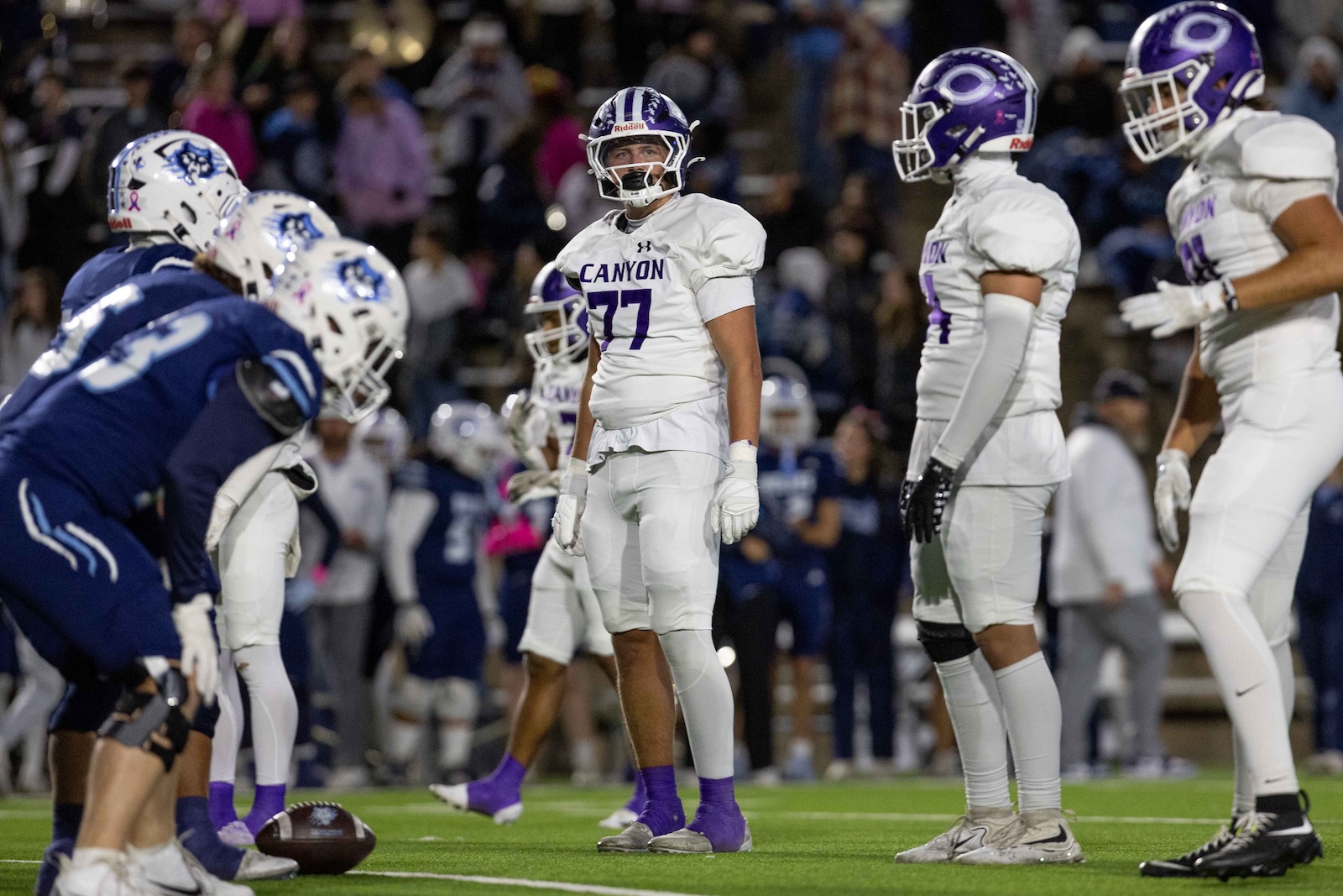 CHS-WPHS-FB-19 | Press Pass Sports College football players on a field meet at line of scrimmage; white team with'CANYON' jerseys centers the scene while opponents in blue line up nearby.