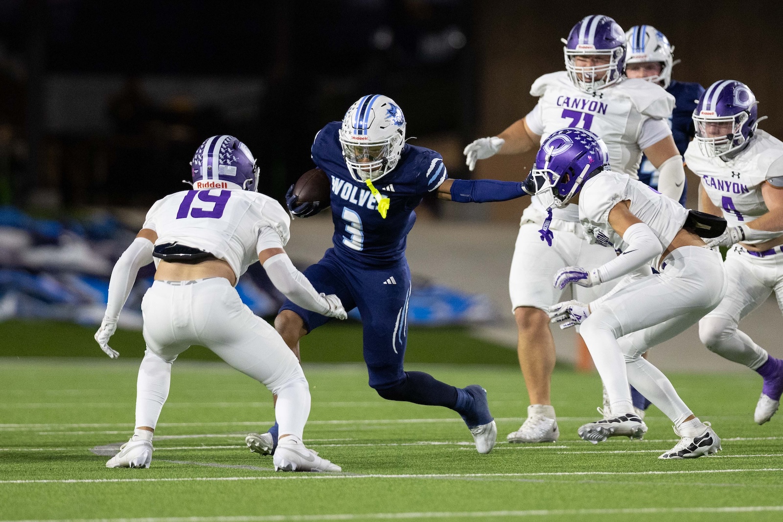 CHS-WPHS-FB-20 | Press Pass Sports Blue team running back with ball evades two Canyon defenders in white on a green field during a football game.