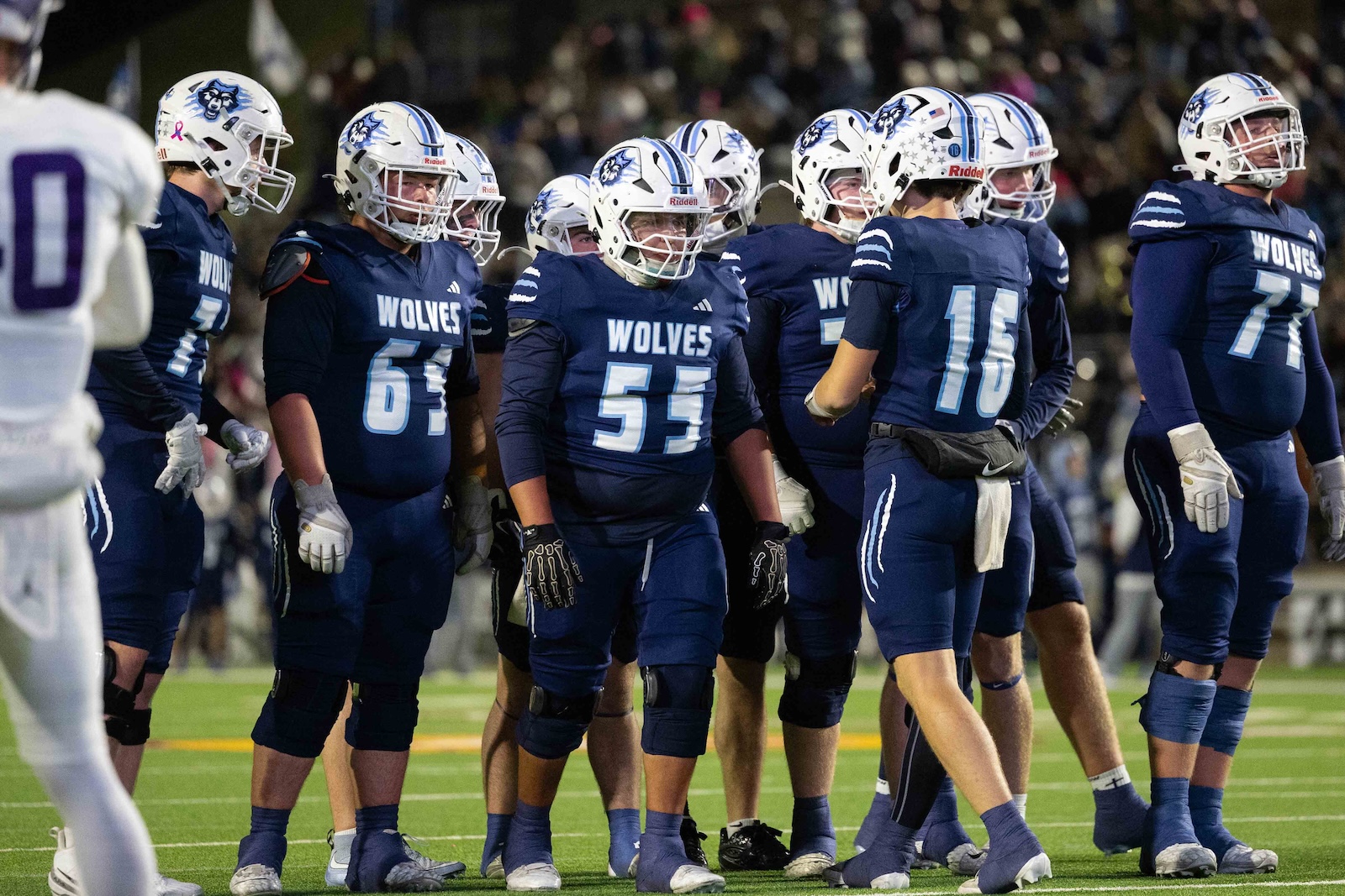 CHS-WPHS-FB-24 | Press Pass Sports Blue-clad high school football players in a huddle on the field, facing inward before a play (WOLVES team).