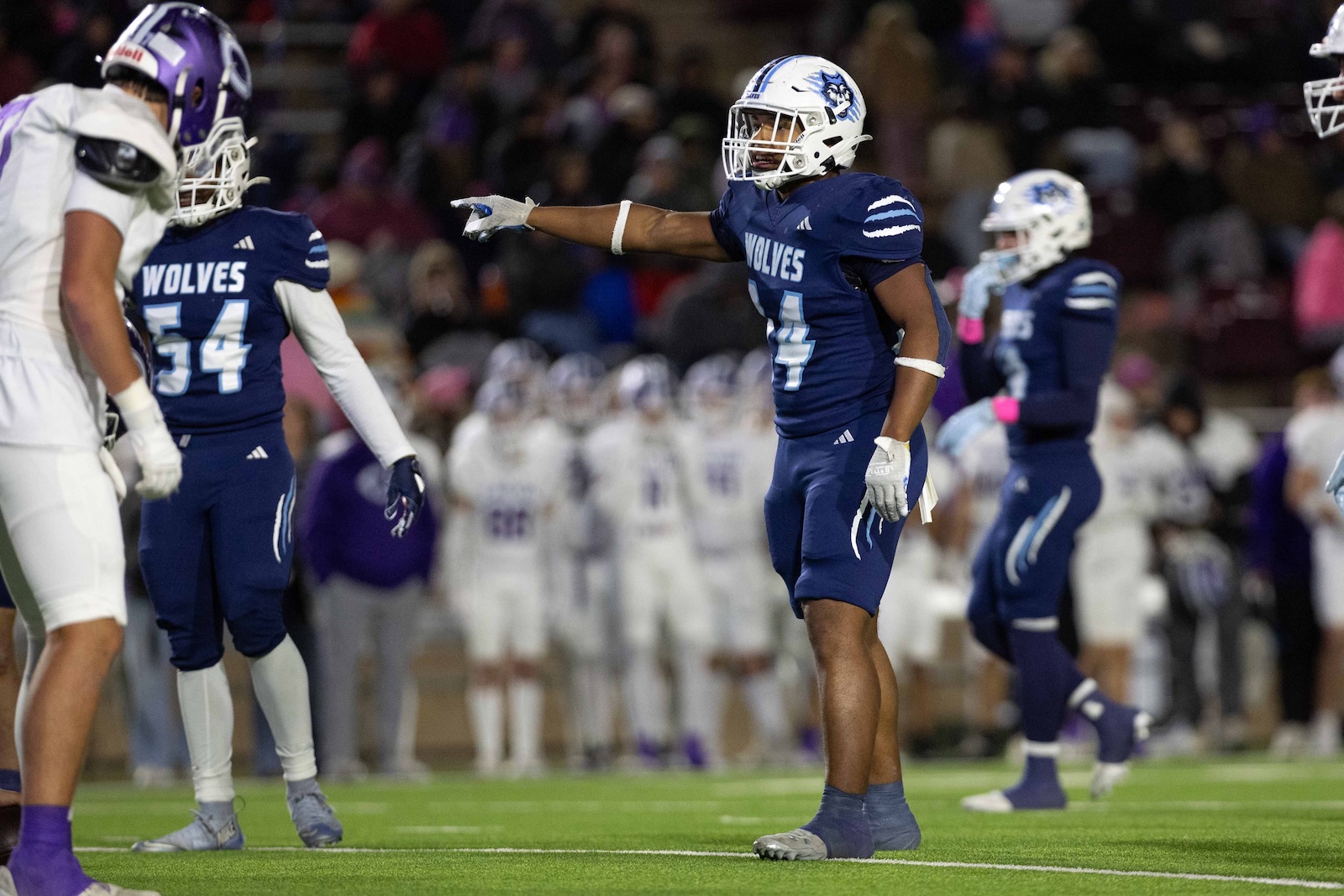 CHS-WPHS-FB-30 | Press Pass Sports Blue Wolves football player pointing downfield during a game on a green turf, teammates nearby.