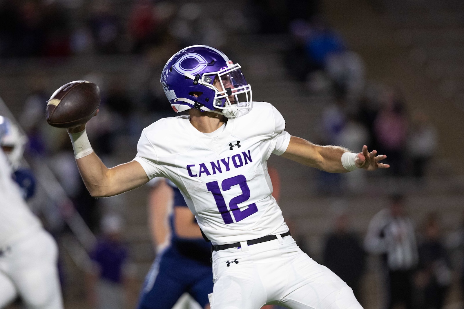 CHS-WPHS-FB-31 | Press Pass Sports Canyon quarterback in a white jersey with purple 12 throws a football during a game under stadium lights