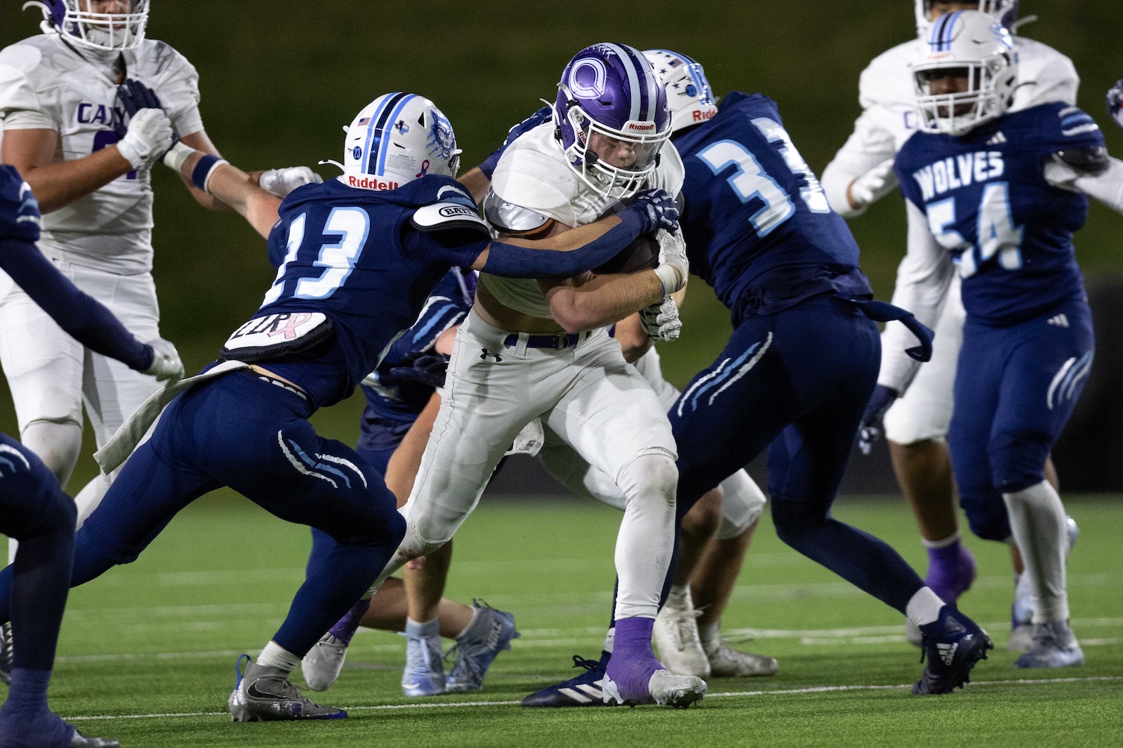 CHS-WPHS-FB-34 | Press Pass Sports White running back tackled by two blue-uniform defenders during a nighttime football game on a turf field.