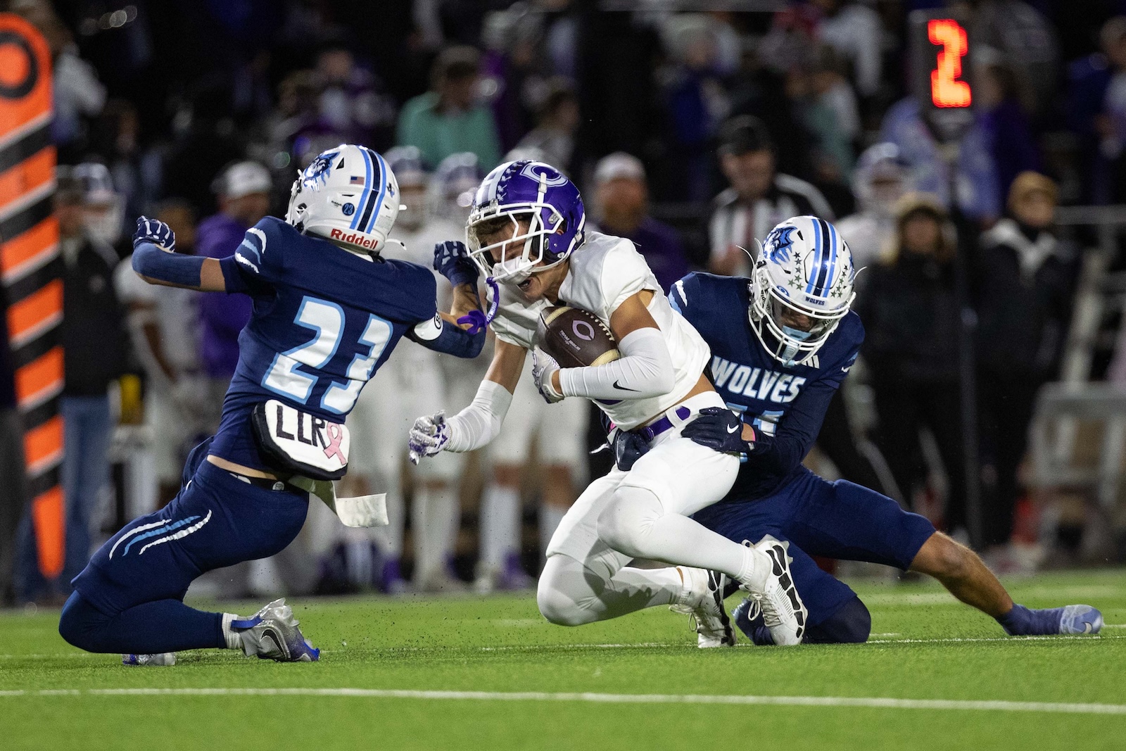 CHS-WPHS-FB-38 | Press Pass Sports Football play: a ball carrier in white evades two tacklers in blue on a green field with a crowded stands background.
