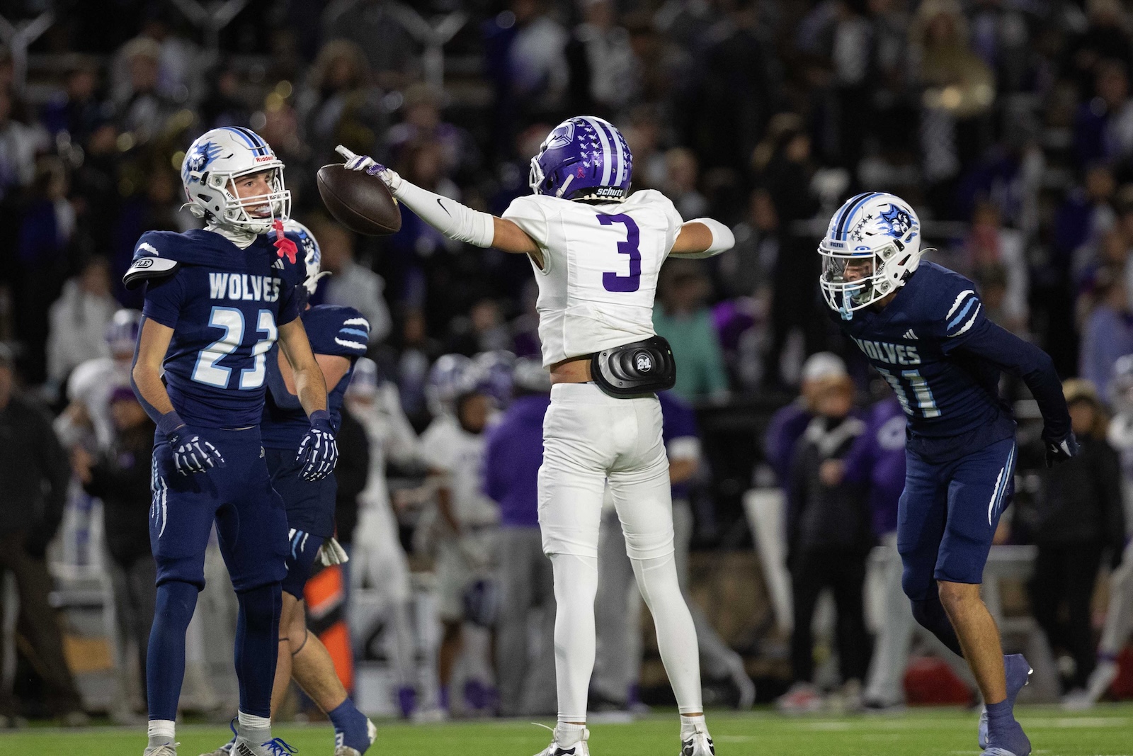 CHS-WPHS-FB-39 | Press Pass Sports Quarterback in white #3 throws a pass as two blue-clad Wolves defenders move in nearby in a packed stadium.