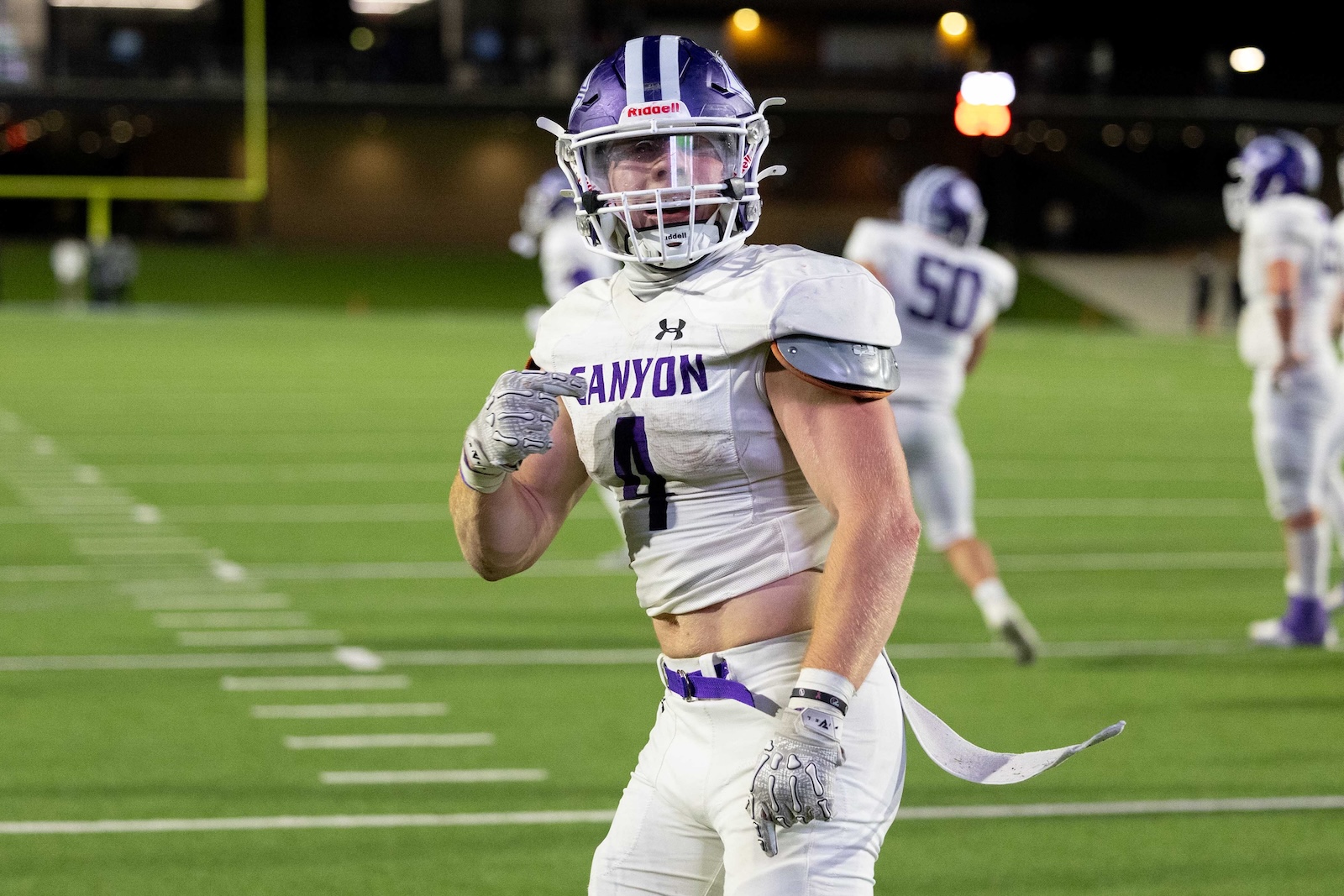 CHS-WPHS-FB-40 | Press Pass Sports Football player from Canyon, wearing a white jersey with purple lettering and number 4, helmet, and gloves on a nighttime turf field.