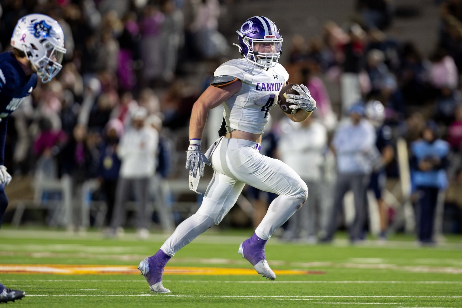 CHS-WPHS-FB-42 | Press Pass Sports Canyon football player in a white jersey runs with the ball during a game, crowd blurred in the background