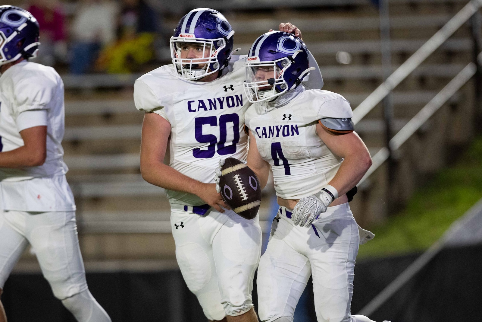 CHS-WPHS-FB-44 | Press Pass Sports Two Canyon football players in white and purple celebrate on the field, one holding a football between them.
