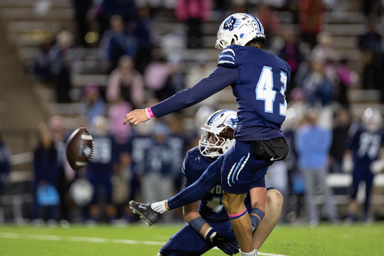 CHS-WPHS-FB-45 | Press Pass Sports Two football players in blue uniforms jump for the ball as a chaotic play unfolds on the field with fans in the stands behind them.