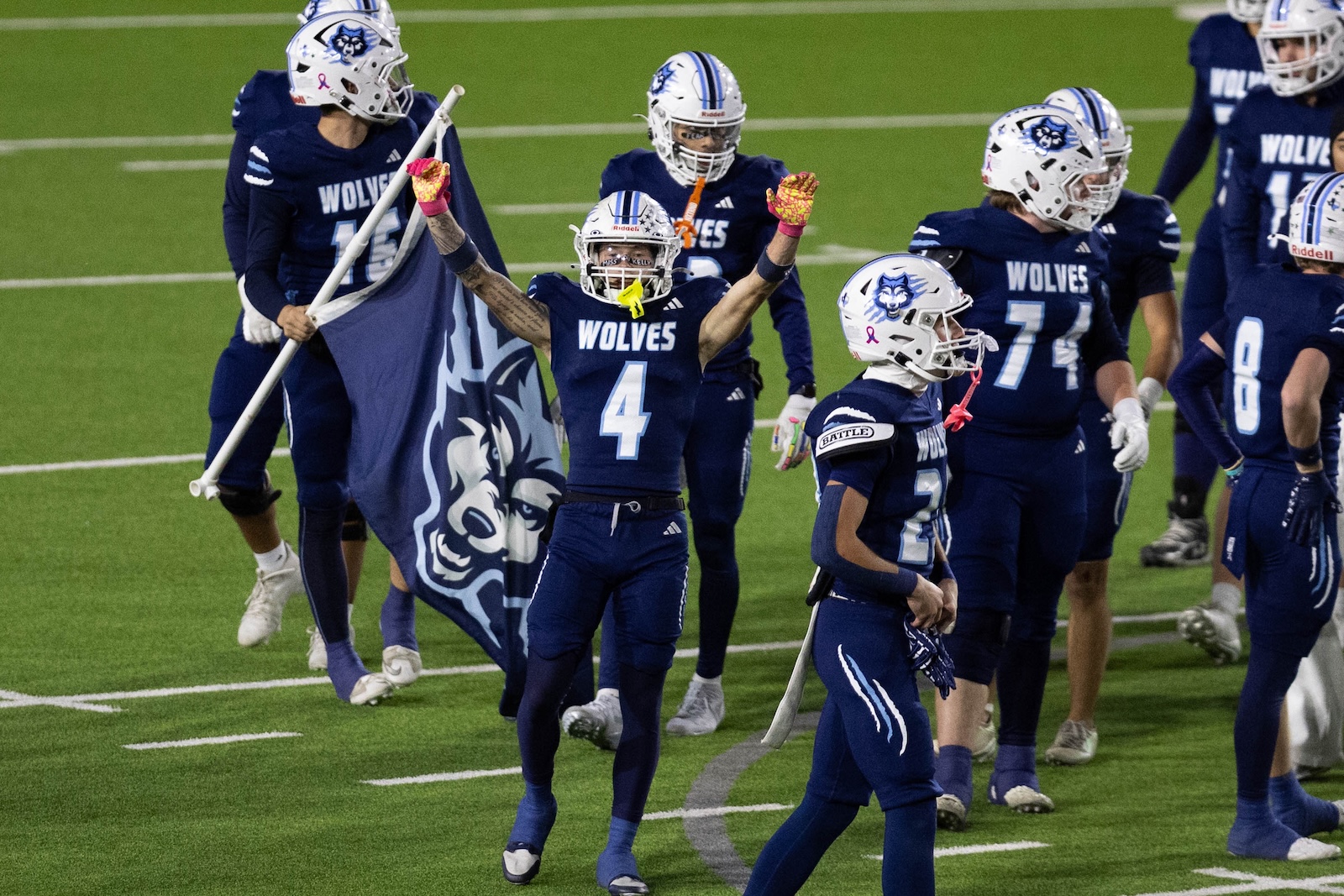 CHS-WPHS-FB-46 | Press Pass Sports Group of Wolves football players in navy uniforms celebrating on the field, center player #4 raises both arms in triumph while teammates surround him.